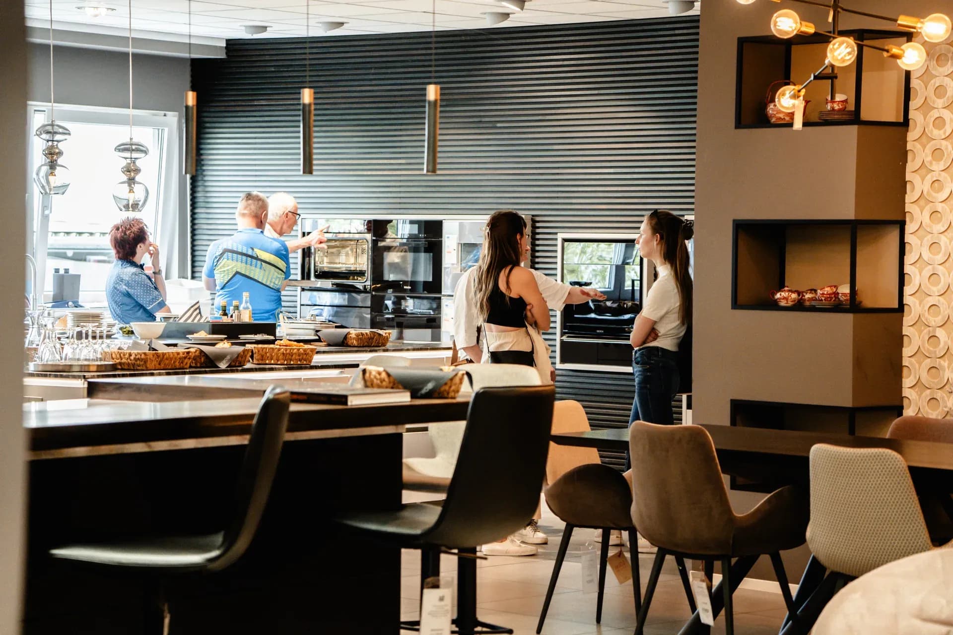 Visiteurs devant le mur d'appareils avec fours dans le showroom Frey, au premier plan une table à manger et des chaises