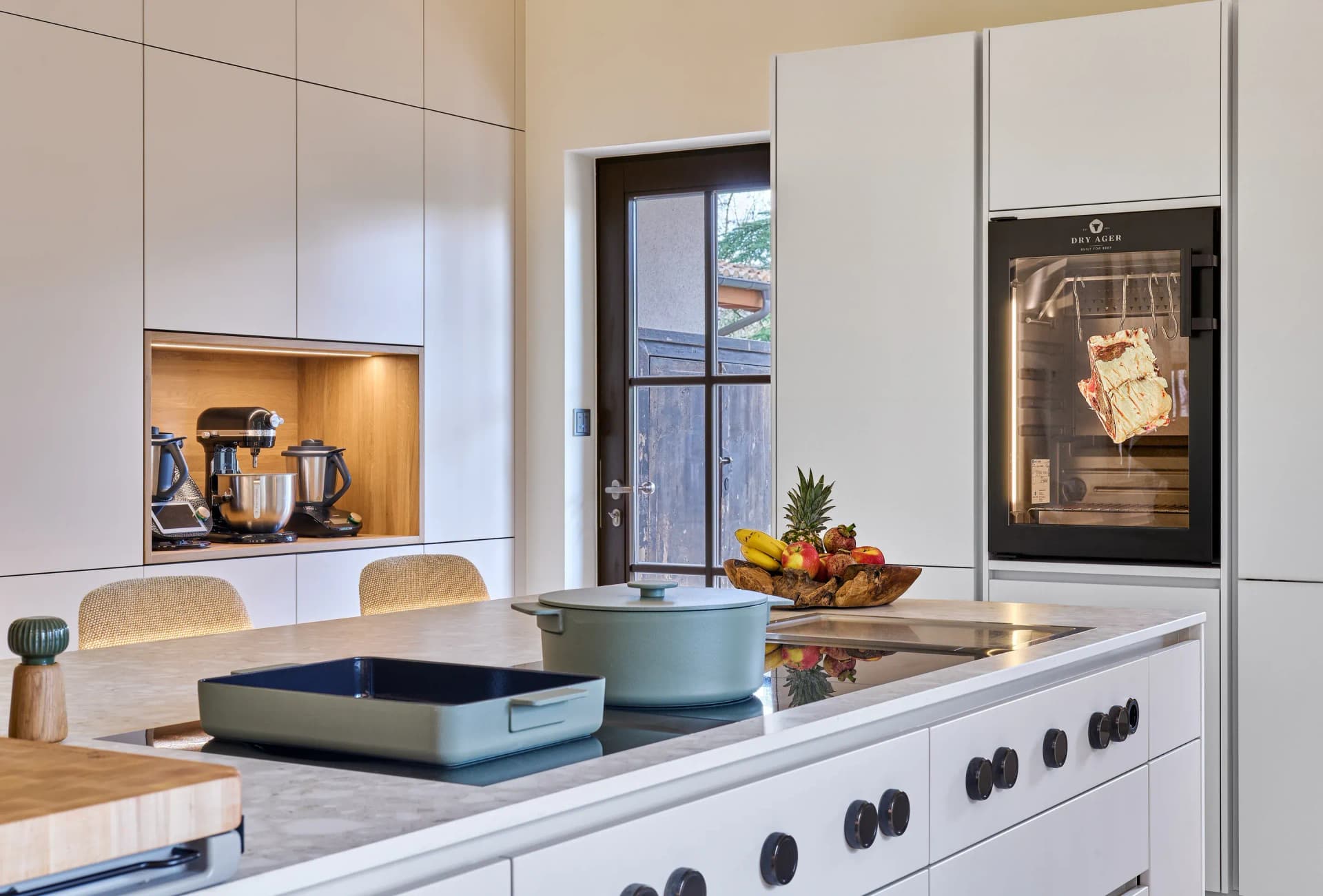 Îlot de cuisson avec plaque, à l'arrière le Dry Ager et une niche éclairée pour les appareils.