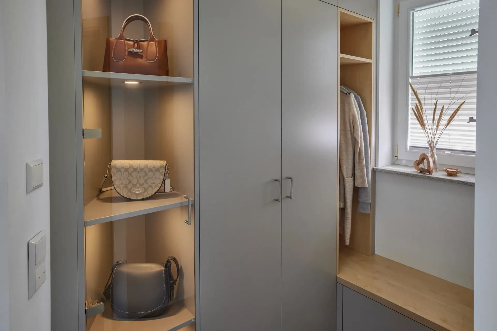 Vestiaire sur mesure avec niches vitrées éclairées pour sacs à main, portes d'armoire grises et niche ouverte en chêne