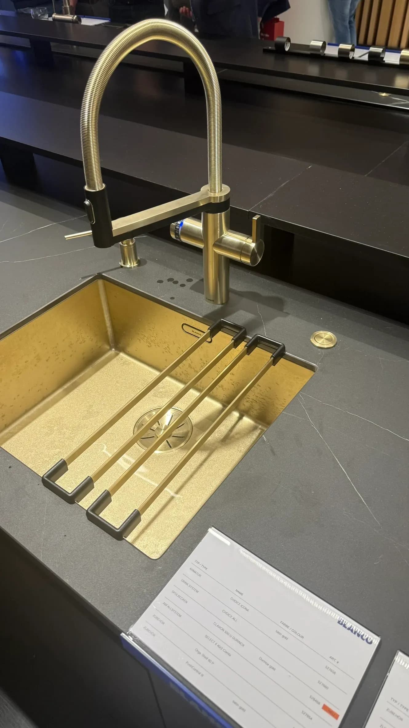 Chez Blanco au Gut Böckel, à la Küchenmeile 2026 : évier CLARON 500-U en DURINOX or avec le mitigeur CHOICE ICONA en satin gold, au premier plan la fiche produit.