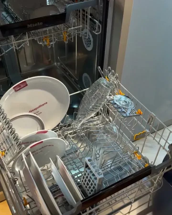 Stand Miele à la Küchenmeile 2026 : lave-vaisselle ouvert, assiettes et verres rangés dans le panier inférieur sorti.
