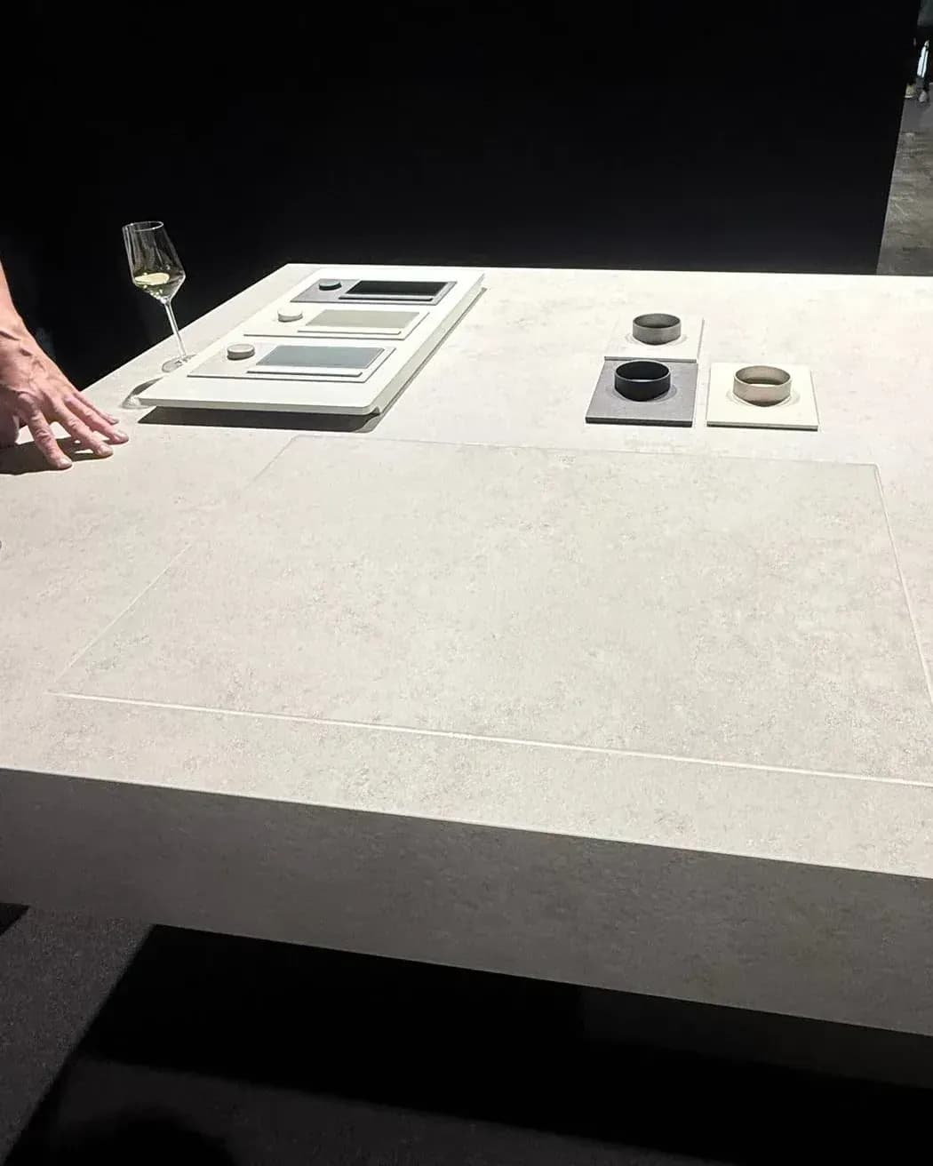 Présenté par V-ZUG dans l’Architekturwerkstatt de LEICHT à Löhne, à la Küchenmeile 2026 : table à surface minérale claire et continue, où la table de cuisson CookTop V6000 Integra ne se devine qu’à un fin contour, derrière des échantillons de matériaux et de commandes.