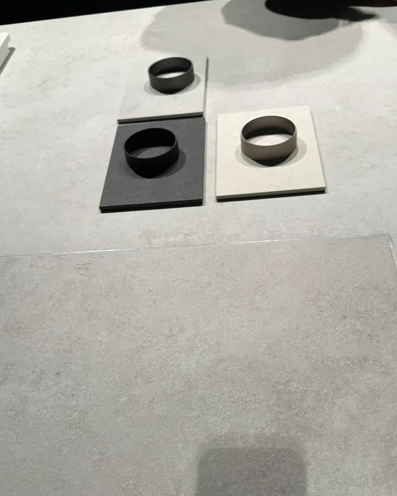 Présenté par V-ZUG dans l’Architekturwerkstatt de LEICHT à Löhne, à la Küchenmeile 2026 : gros plan de la surface minérale claire avec le contour à peine visible de la table de cuisson CookTop V6000 Integra, derrière trois échantillons de matériaux avec anneaux.