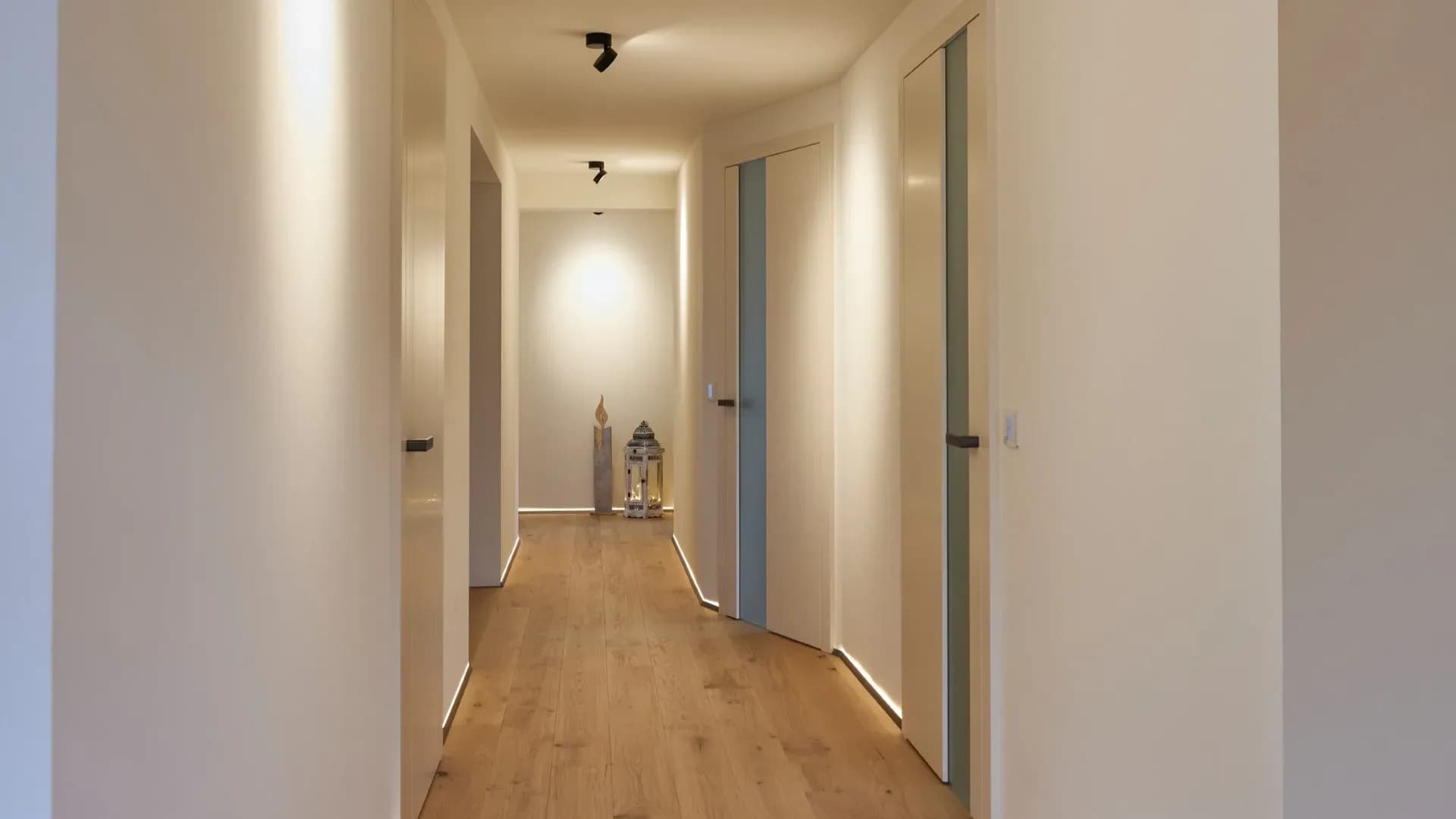 Couloir clair avec portes intérieures blanches affleurantes à fines bandes vitrées sur des lames de chêne huilé