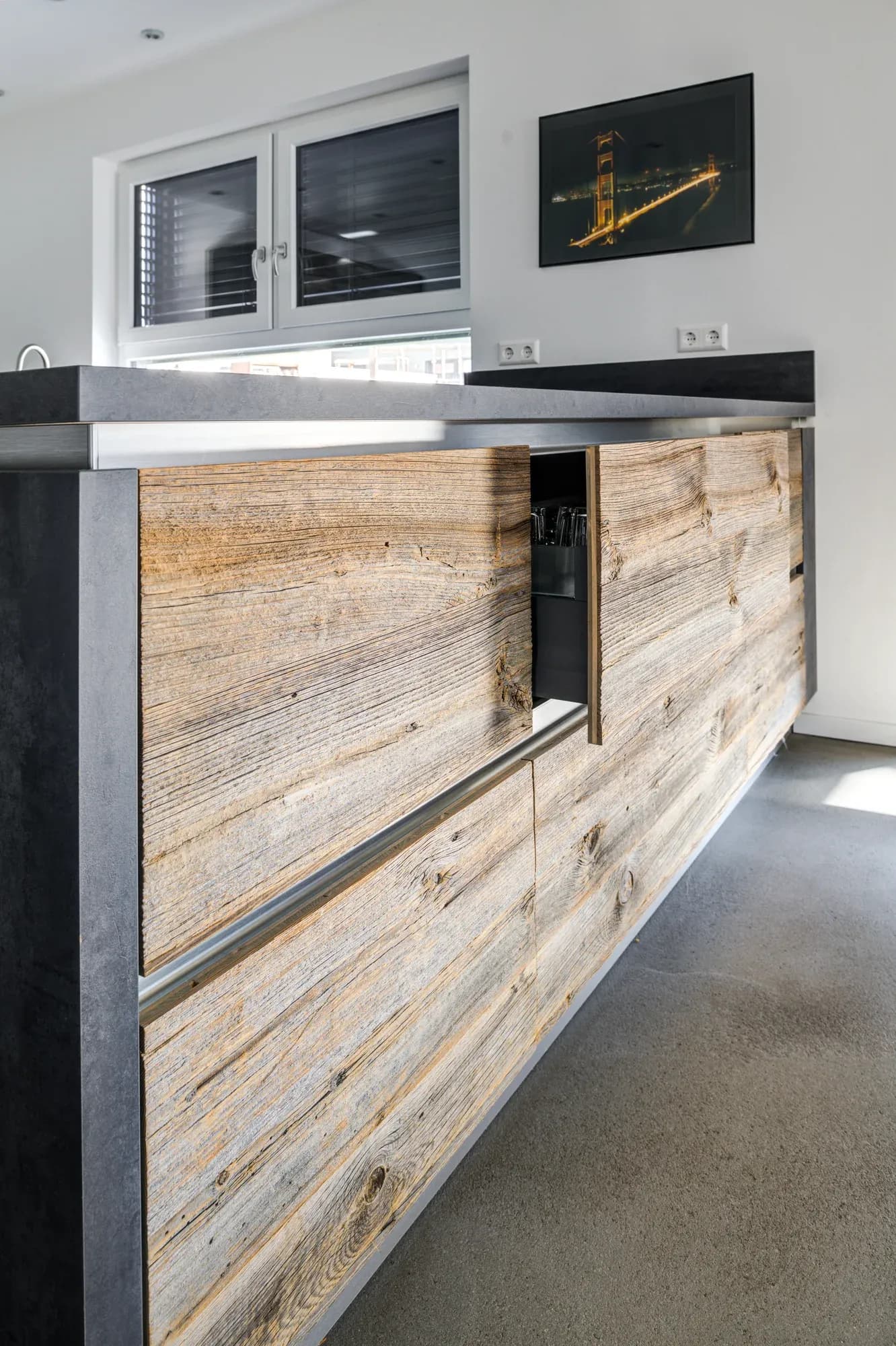 Vue latérale de l'îlot de cuisine avec une façade au look bois ancien vivant et un plan de travail sombre en porte-à-faux