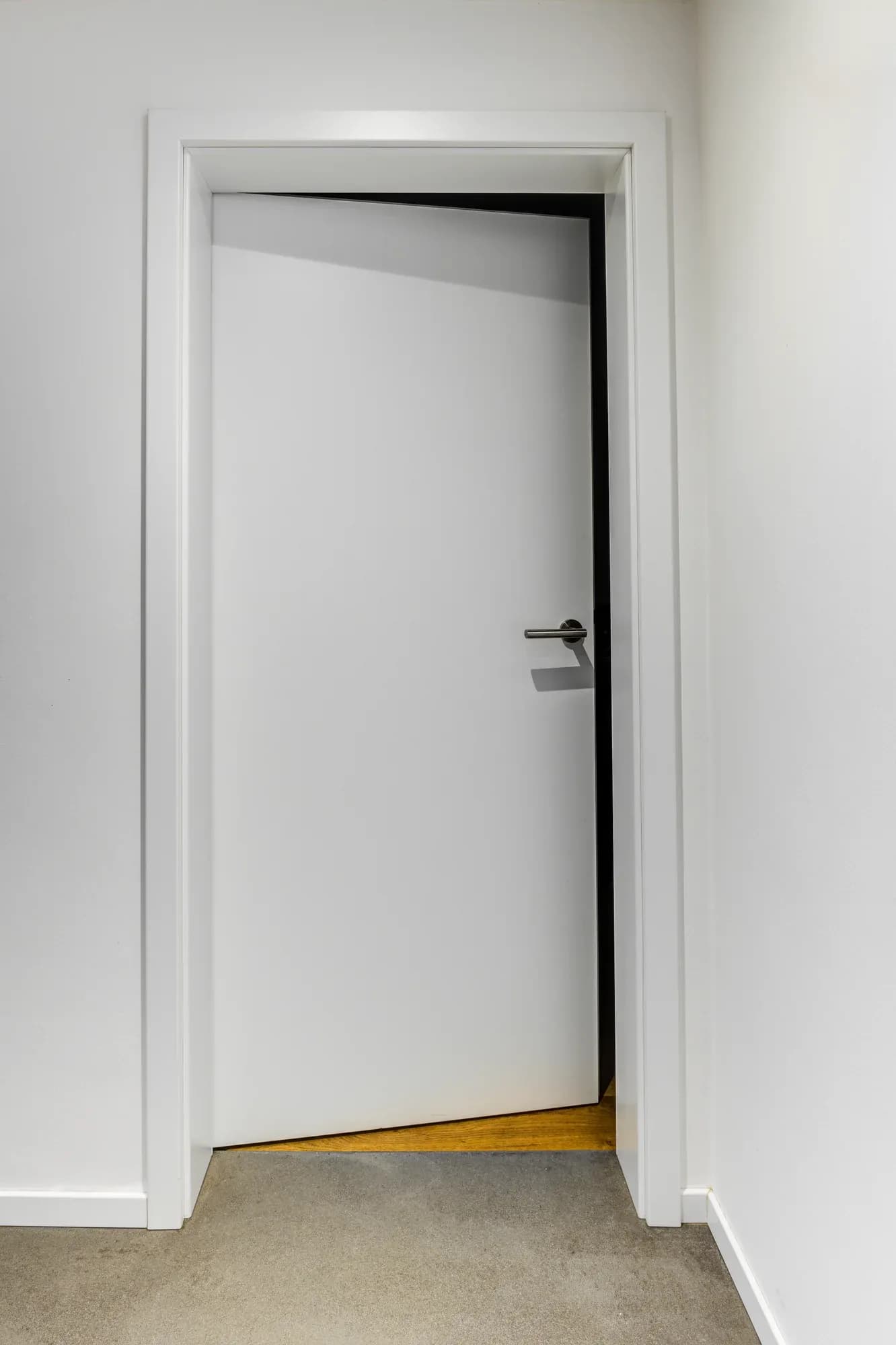 Porte intérieure blanche avec huisserie affleurante à la jonction avec le sol en lames de chêne