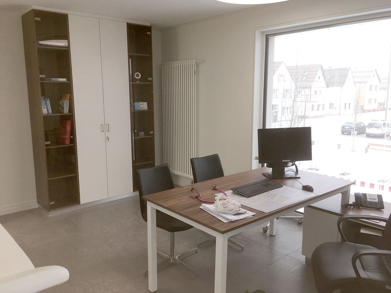Cabinet de consultation avec bureau et armoire toute hauteur à portes vitrées.