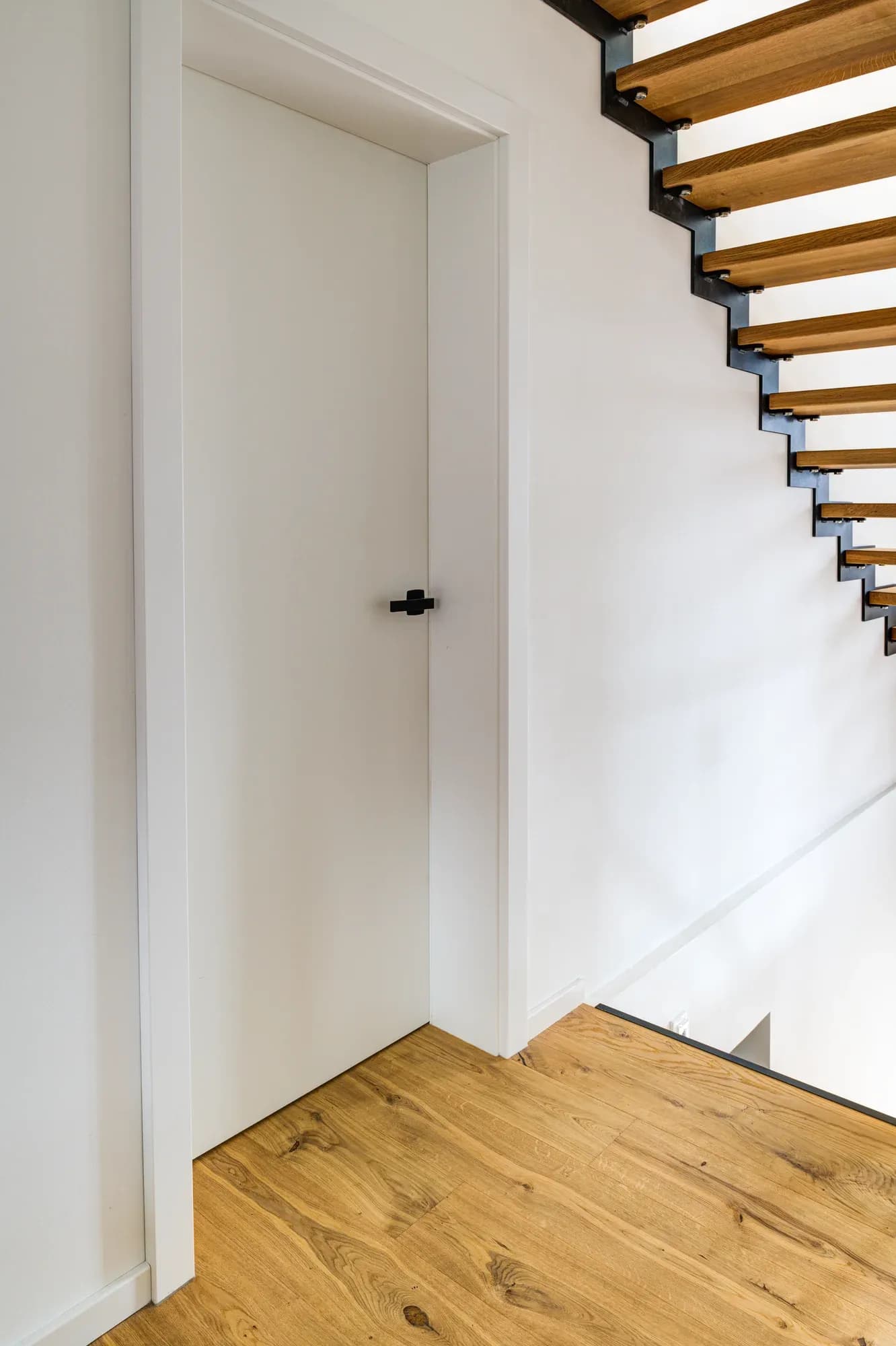 Porte intérieure blanche avec poignée noire mate à côté de la cage d'escalier ouverte