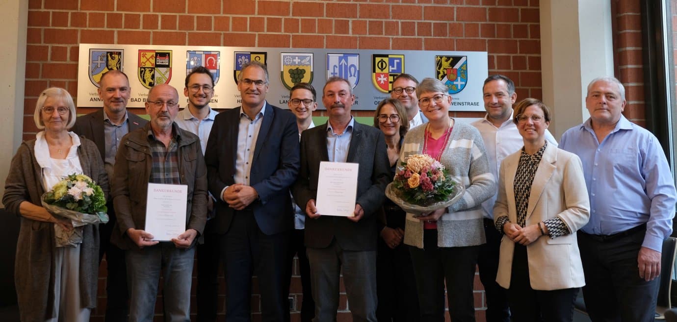 Photo de groupe de la cérémonie au Kreishaus Südliche Weinstraße : Arnold Kolb et Edwin Eichenlaub avec des certificats de remerciement et des fleurs, entourés d'invités d'honneur
