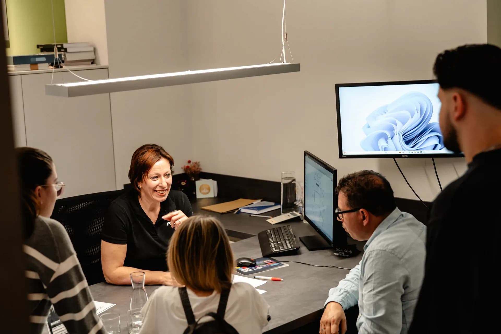 Conseillère Frey en discussion avec trois clients à la table de conception, à côté l'écran avec le plan de la cuisine