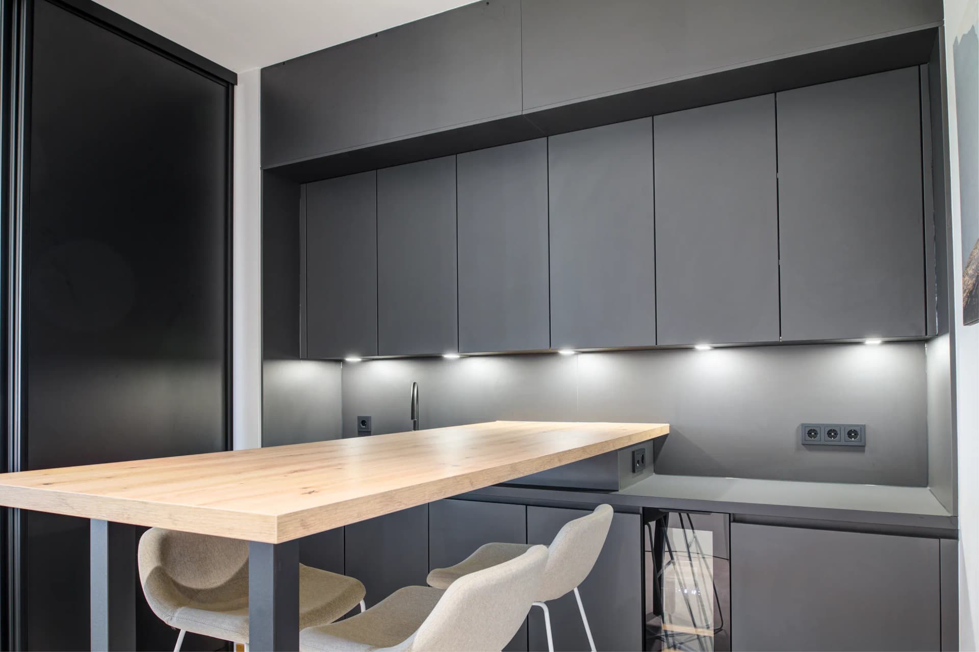 Linéaire de cuisine anthracite avec éclairage sous les meubles et table haute attenante.
