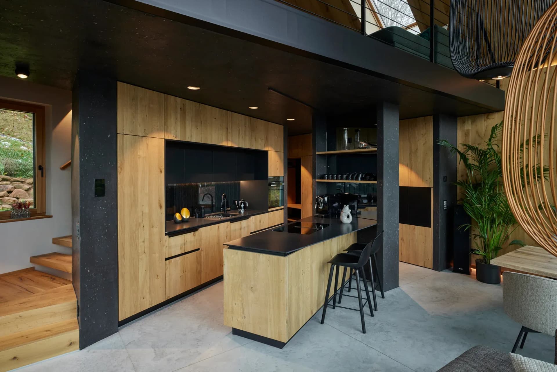Îlot de cuisine en chêne et noir avec tabourets de bar, escalier et plante verte en arrière-plan