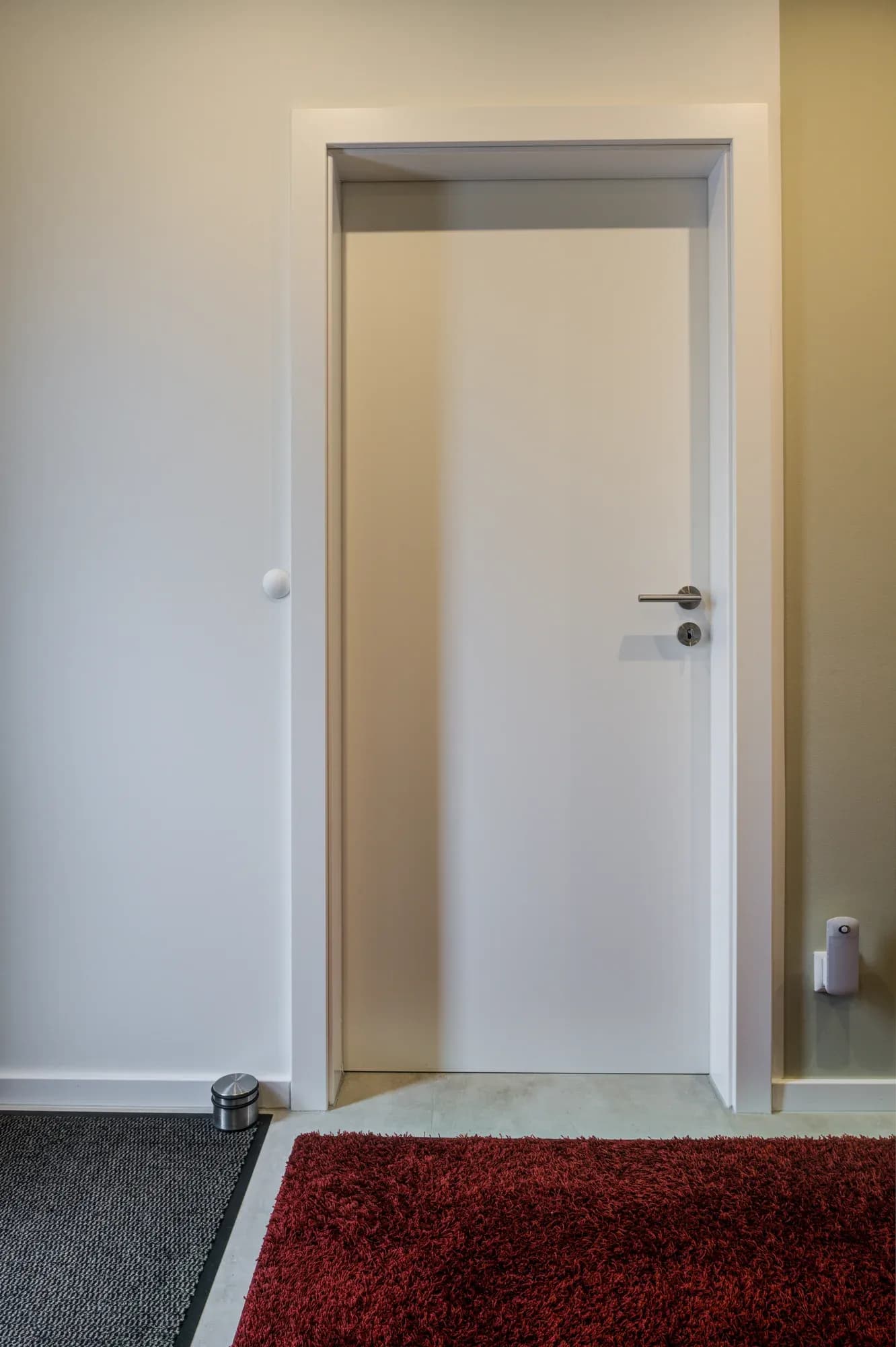Porte intérieure blanche avec huisserie affleurante, avec un tapis rouge devant