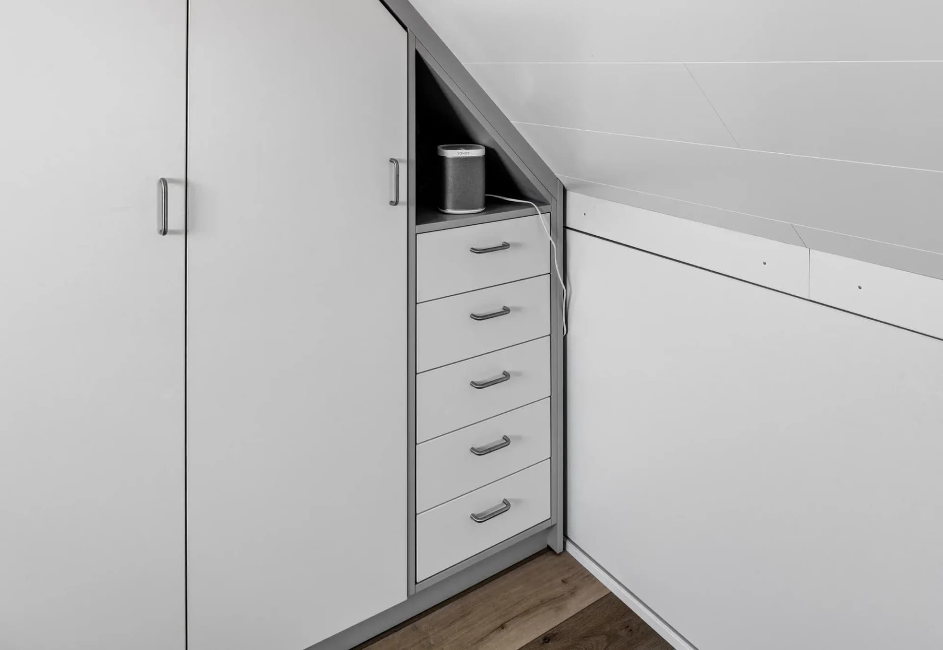 Détail d'un placard sous la pente du toit : niche ouverte avec enceinte au-dessus d'une colonne de tiroirs ; à droite, des rangements bas le long du mur d'appui.