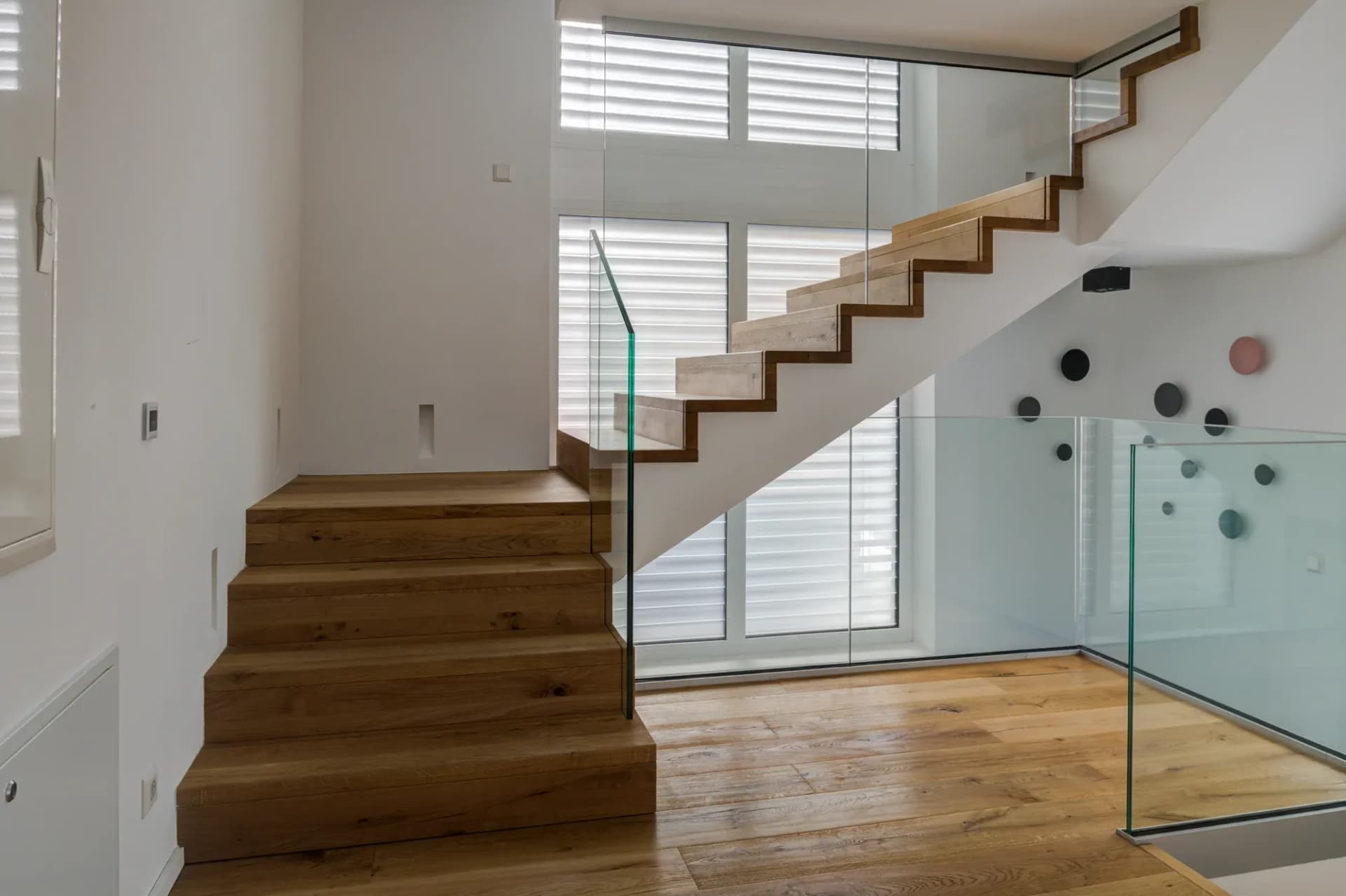L'escalier en chêne à structure pliée monte tout droit vers l'étage, avec une rambarde en verre sur le côté.