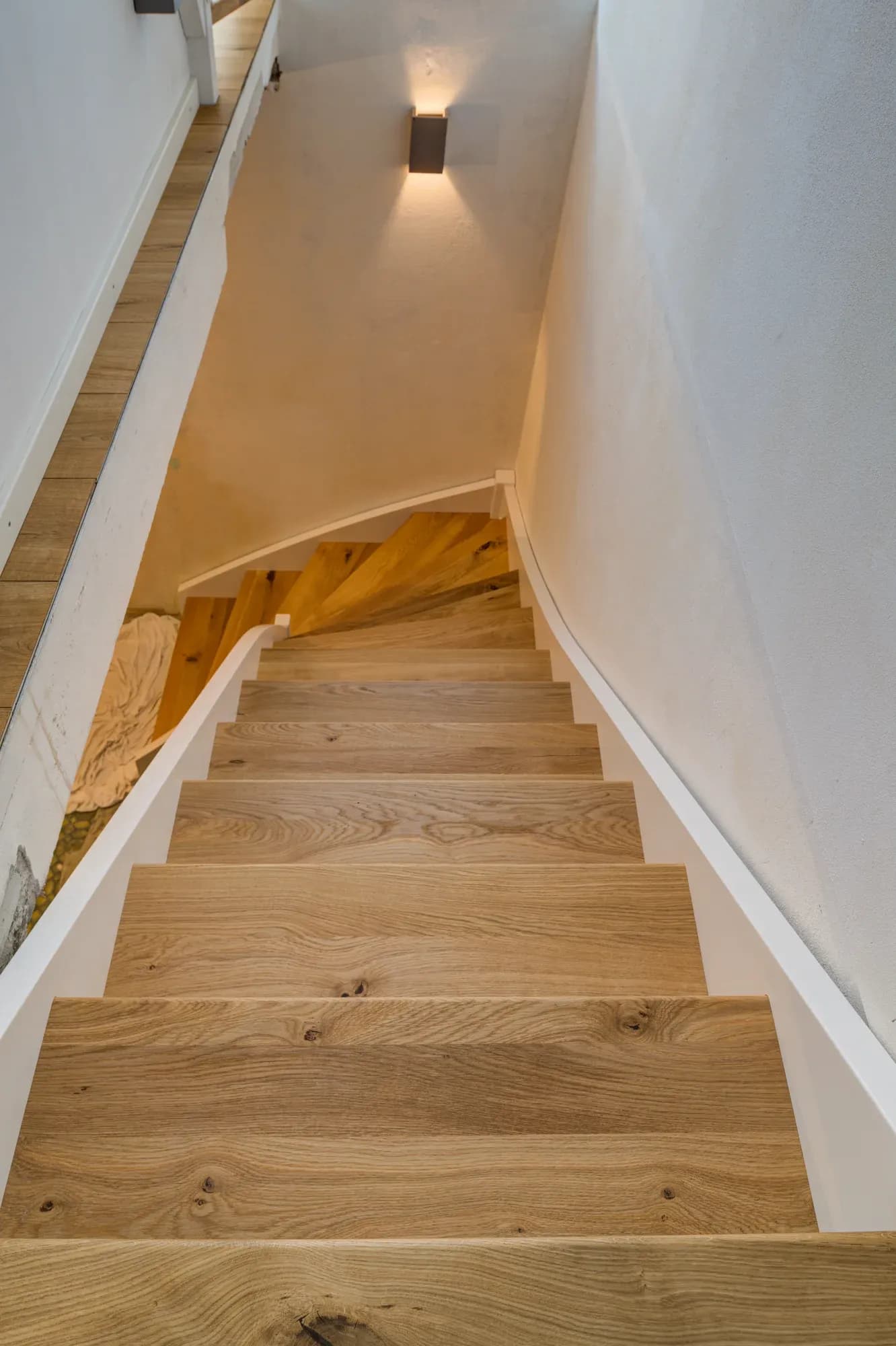 Escalier en chêne sous les combles, marches ouvertes en chêne noueux entre des murs blancs