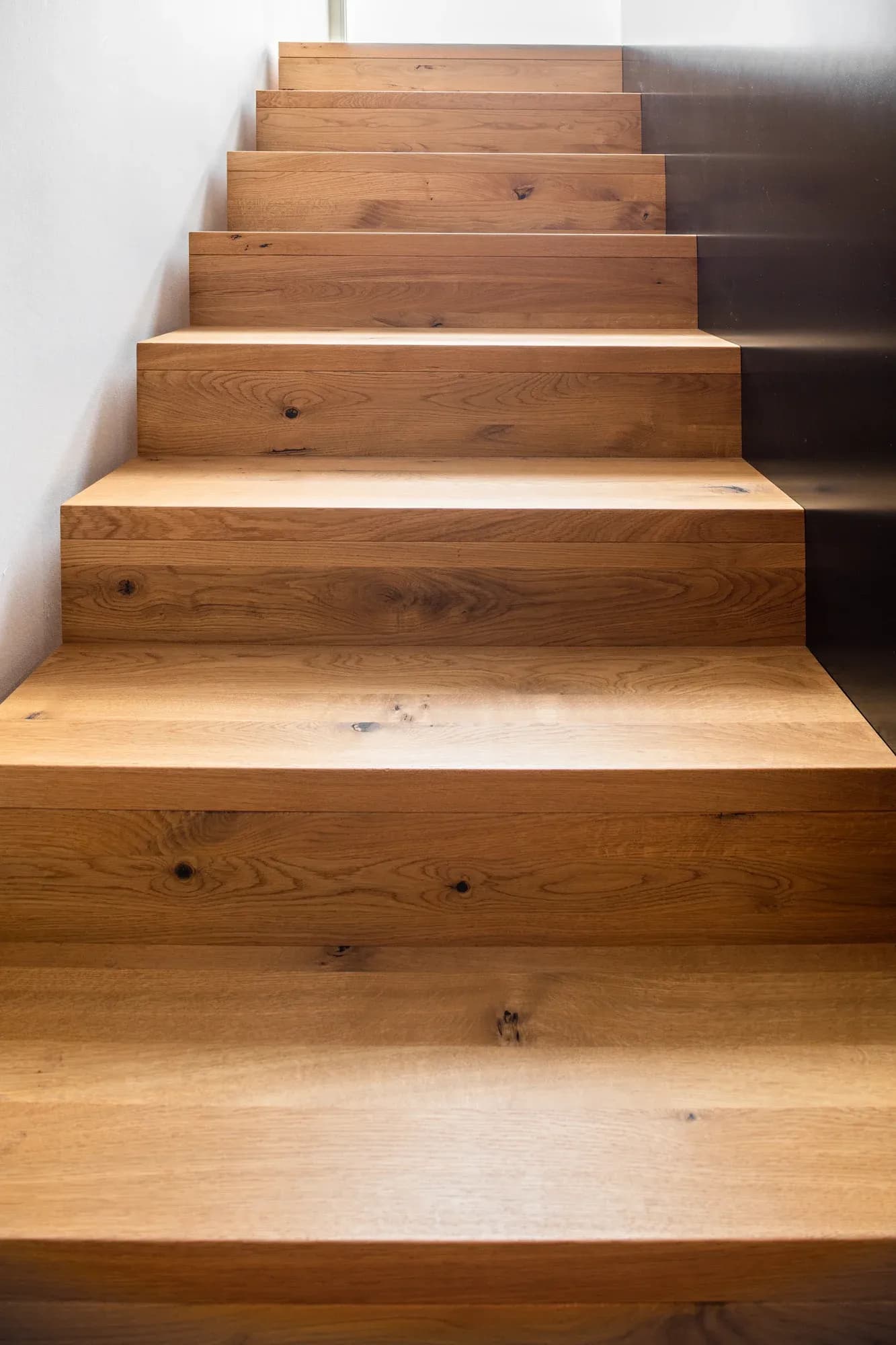 Vue vers le haut de l'escalier en chêne : marches massives en chêne noueux et limon en acier noir.