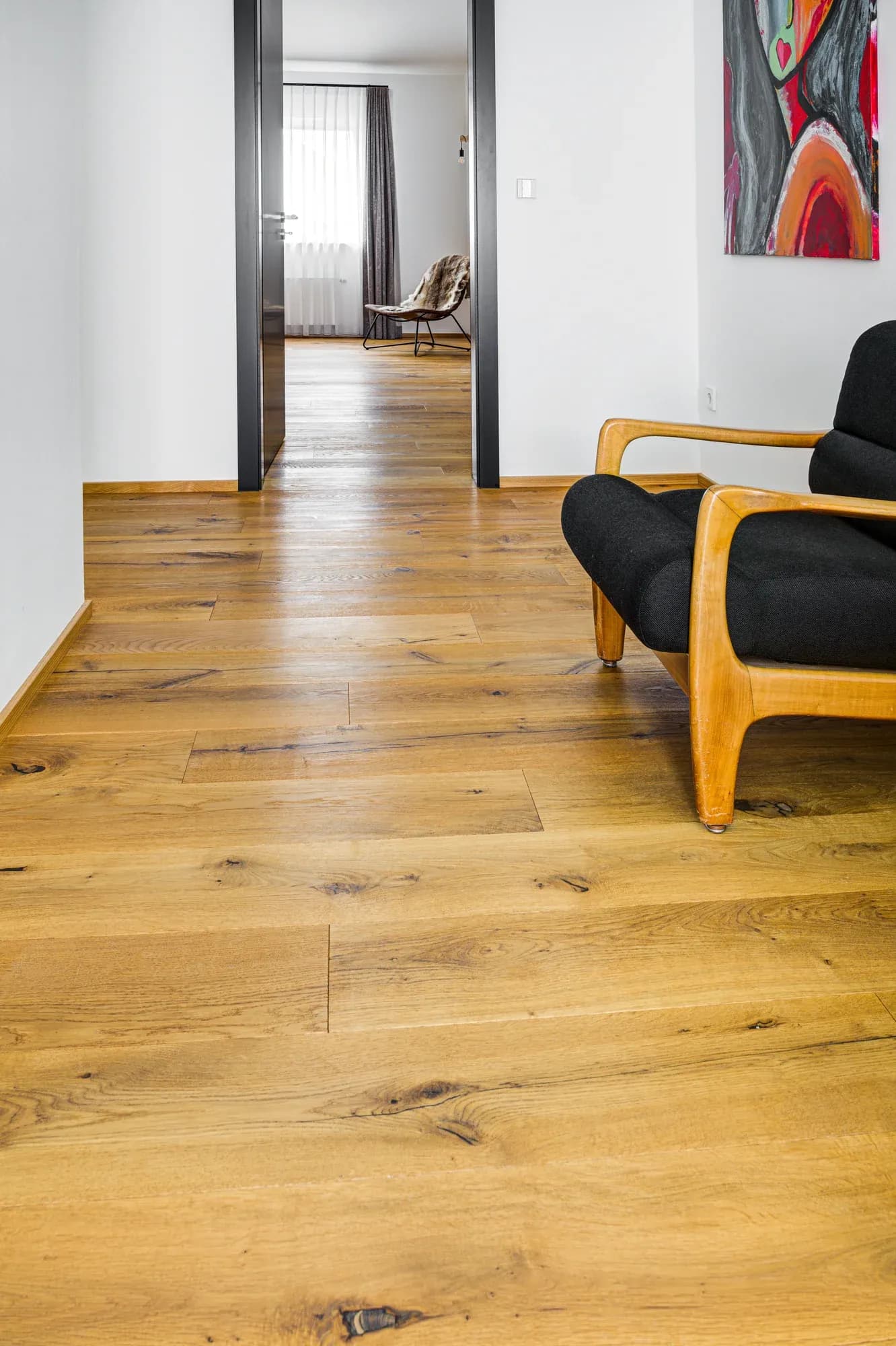 Large parquet en chêne noueux dans le couloir, encadré de chambranles de porte noirs.
