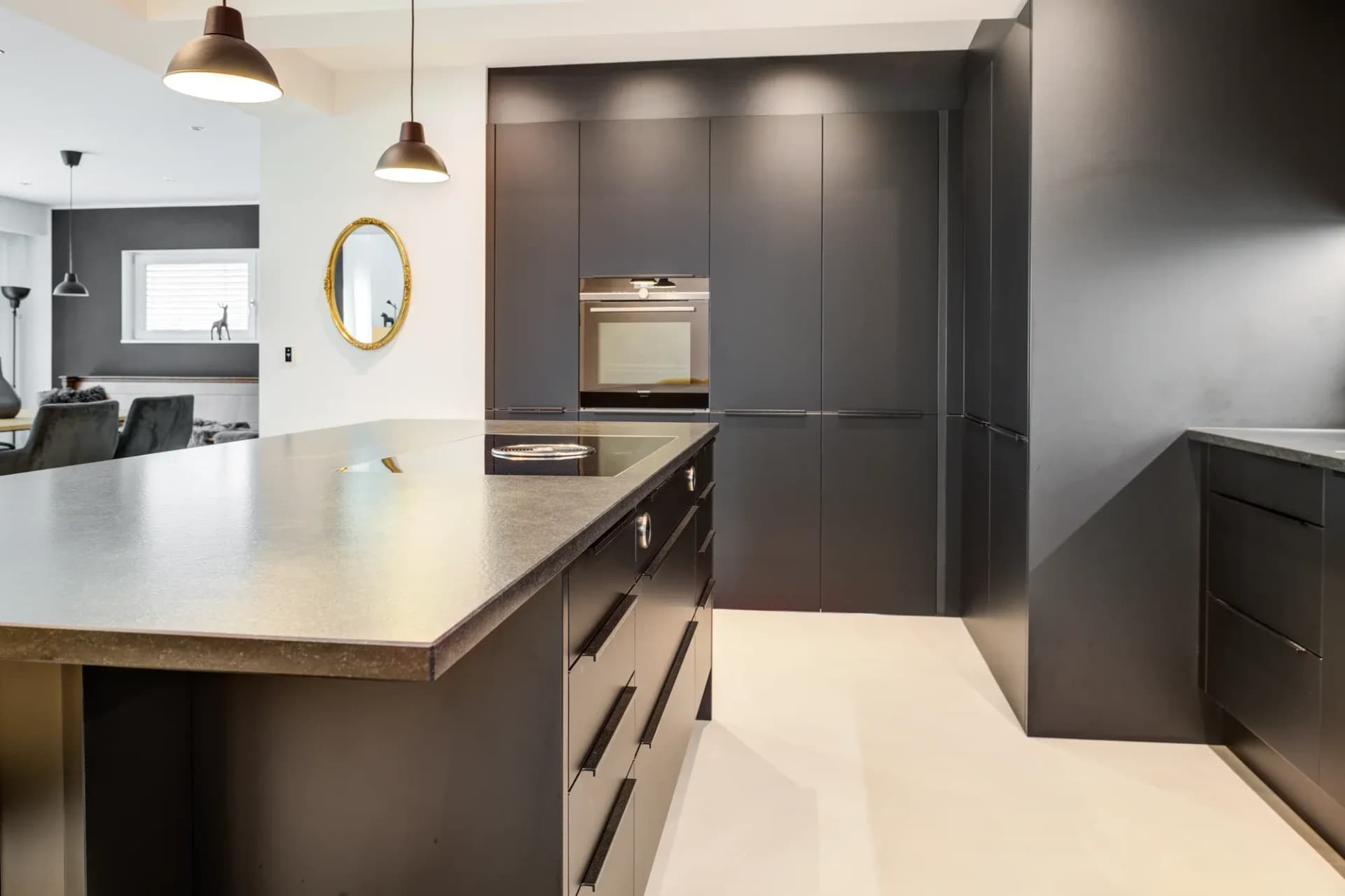 Cuisine noire avec îlot de cuisson et plan de travail effet pierre, vue sur le séjour attenant.