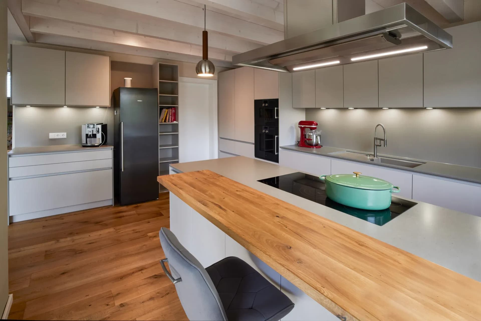 Îlot de cuisine avec plan de travail en chêne massif, table de cuisson à induction et réfrigérateur noir dans la cuisine ouverte.