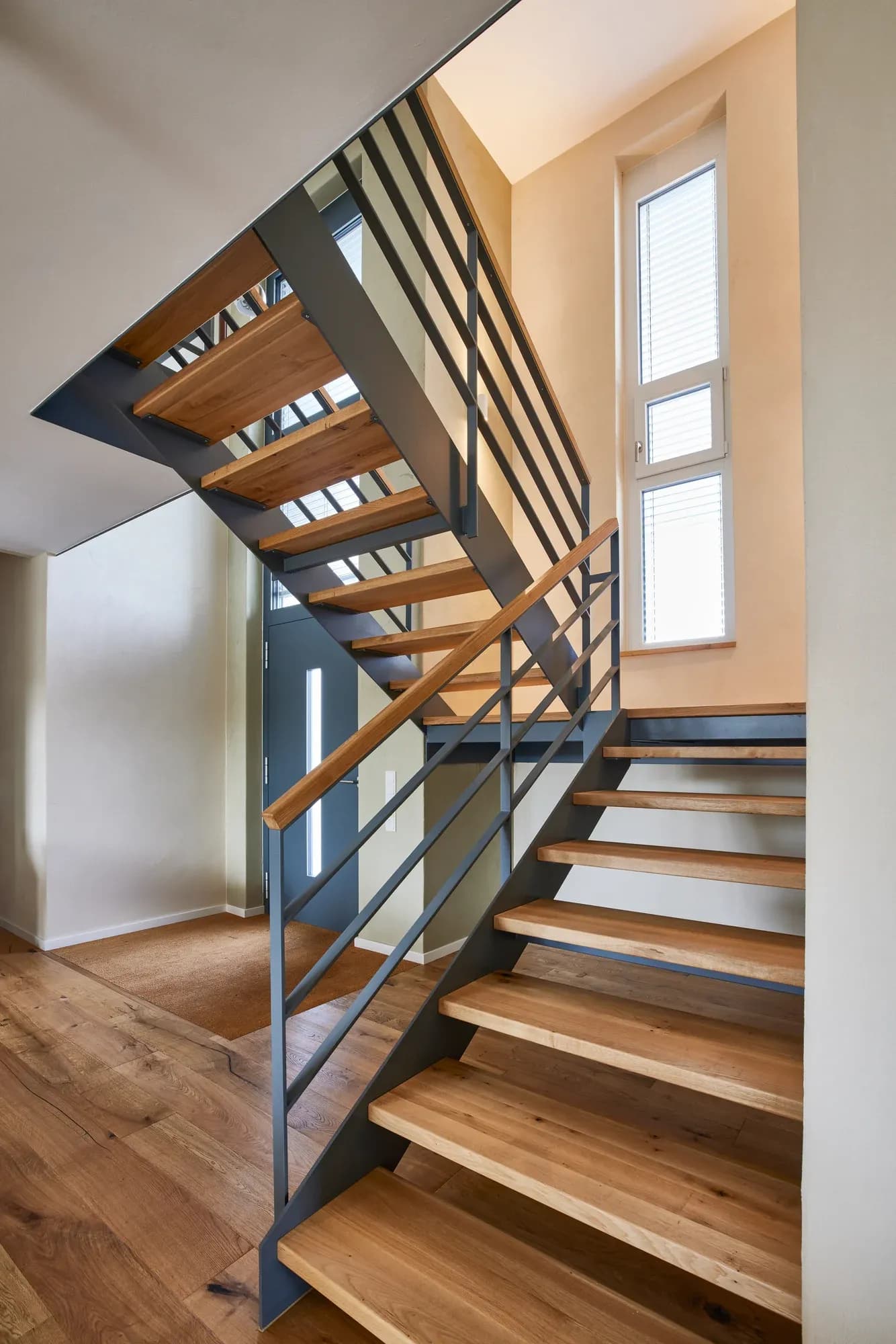 Escalier ouvert en acier plat noir avec marches en chêne près de la fenêtre.