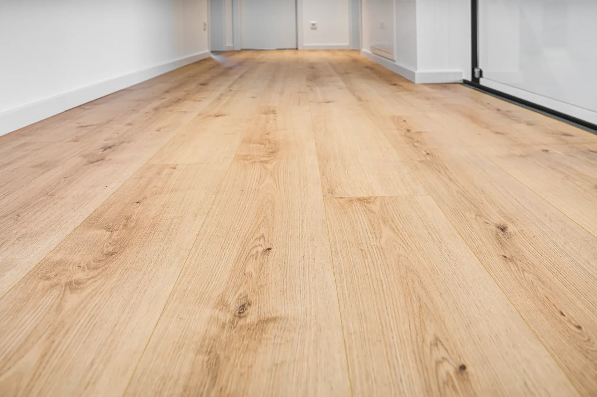 Séjour lumineux avec parquet en chêne continu et baie vitrée toute hauteur à cadre foncé.