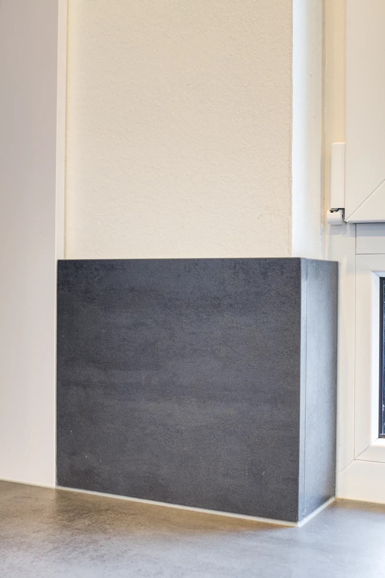 Bloc séparateur bas habillé de céramique foncée devant un mur blanc, sur un sol en chêne clair.