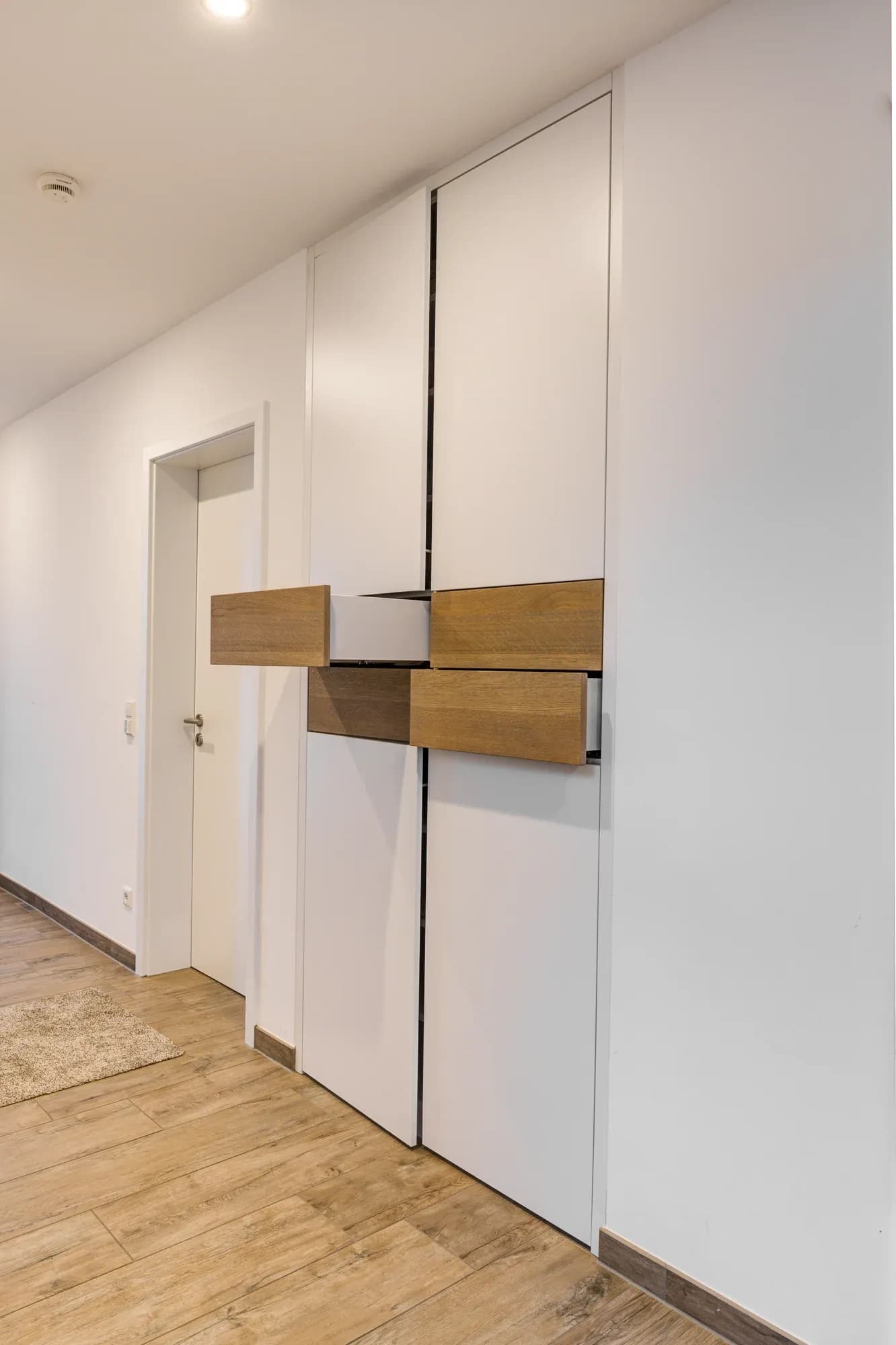 Armoires encastrées blanches toute hauteur dans un couloir avec console suspendue en chêne et porte intérieure blanche sur un sol en chêne.