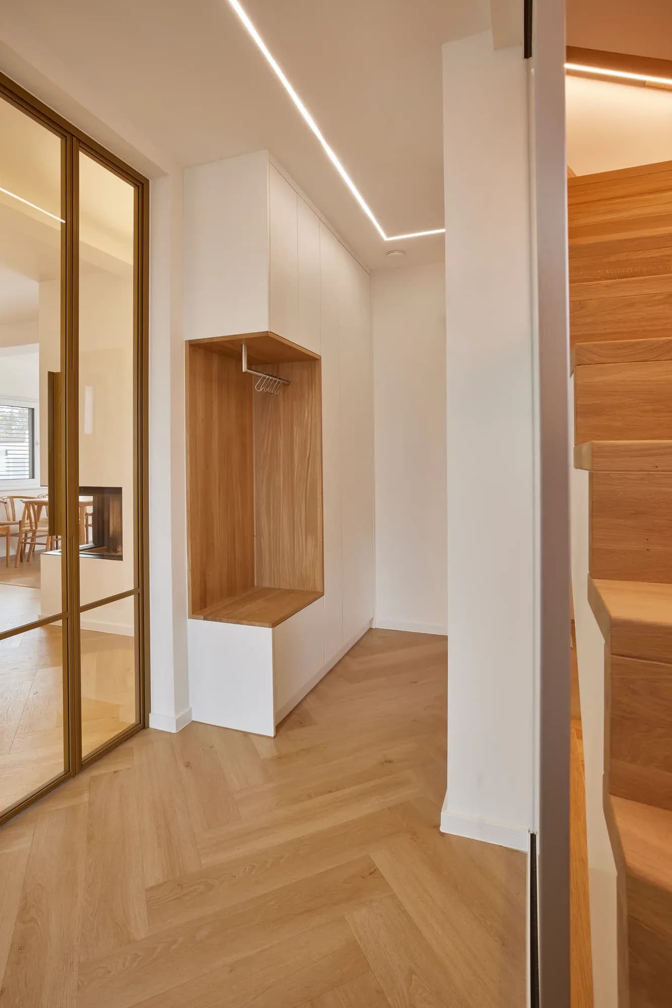Niche à vestiaire intégrée en chêne avec banc, à côté une porte miroir au cadre couleur laiton et l'escalier.
