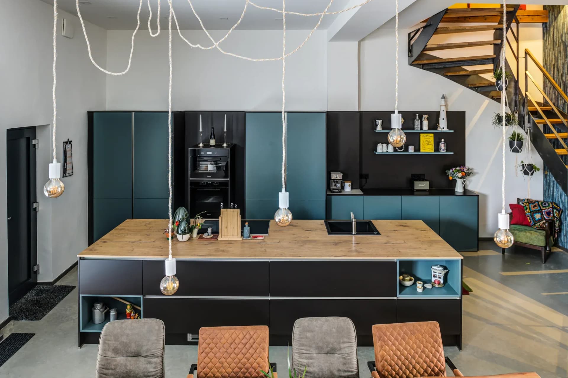 Espace de vie ouvert avec table à manger, îlot de cuisine bleu pétrole et escalier à l'arrière-plan.