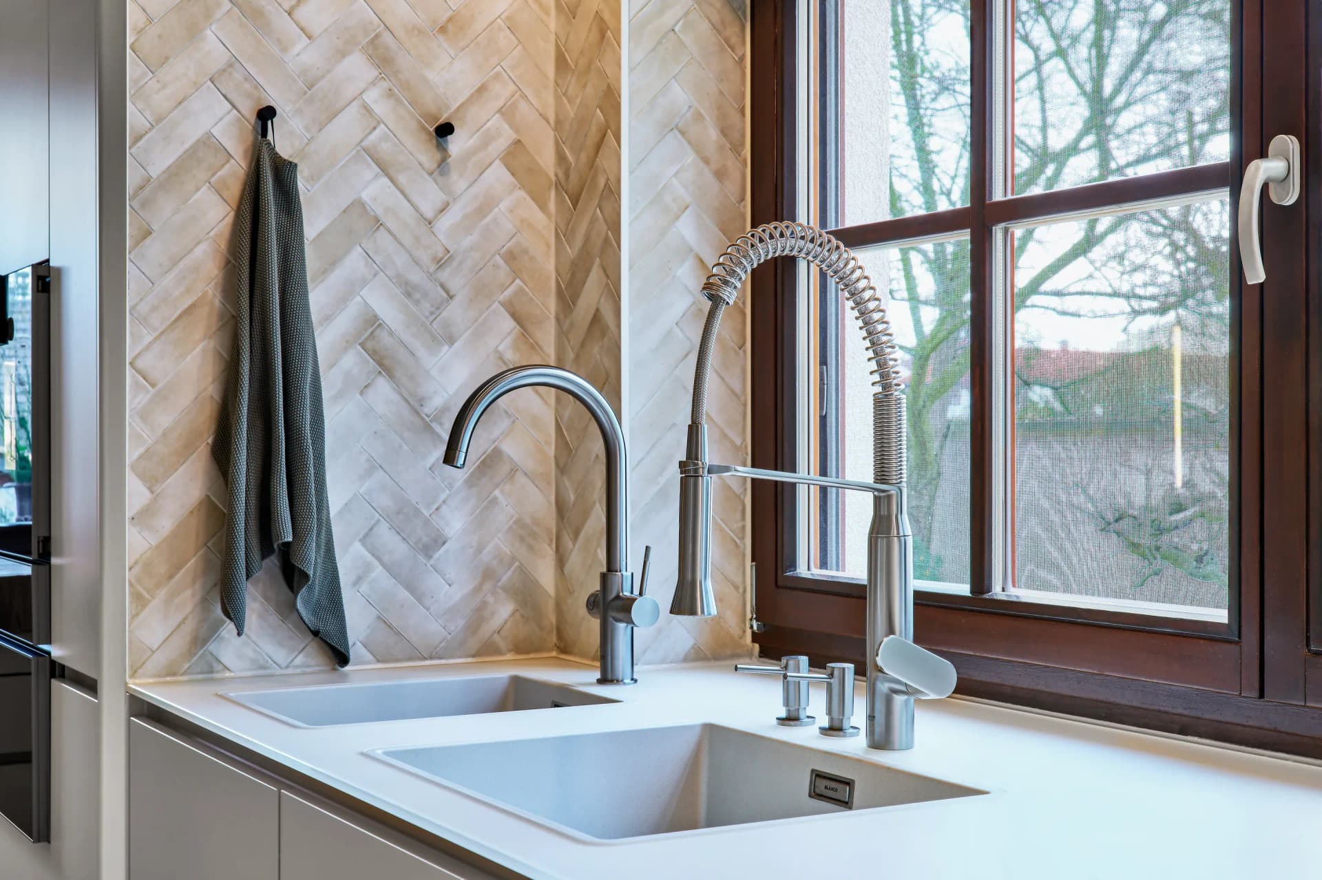 Double évier avec douchette professionnelle devant la fenêtre, carrelage à chevrons en arrière-plan.