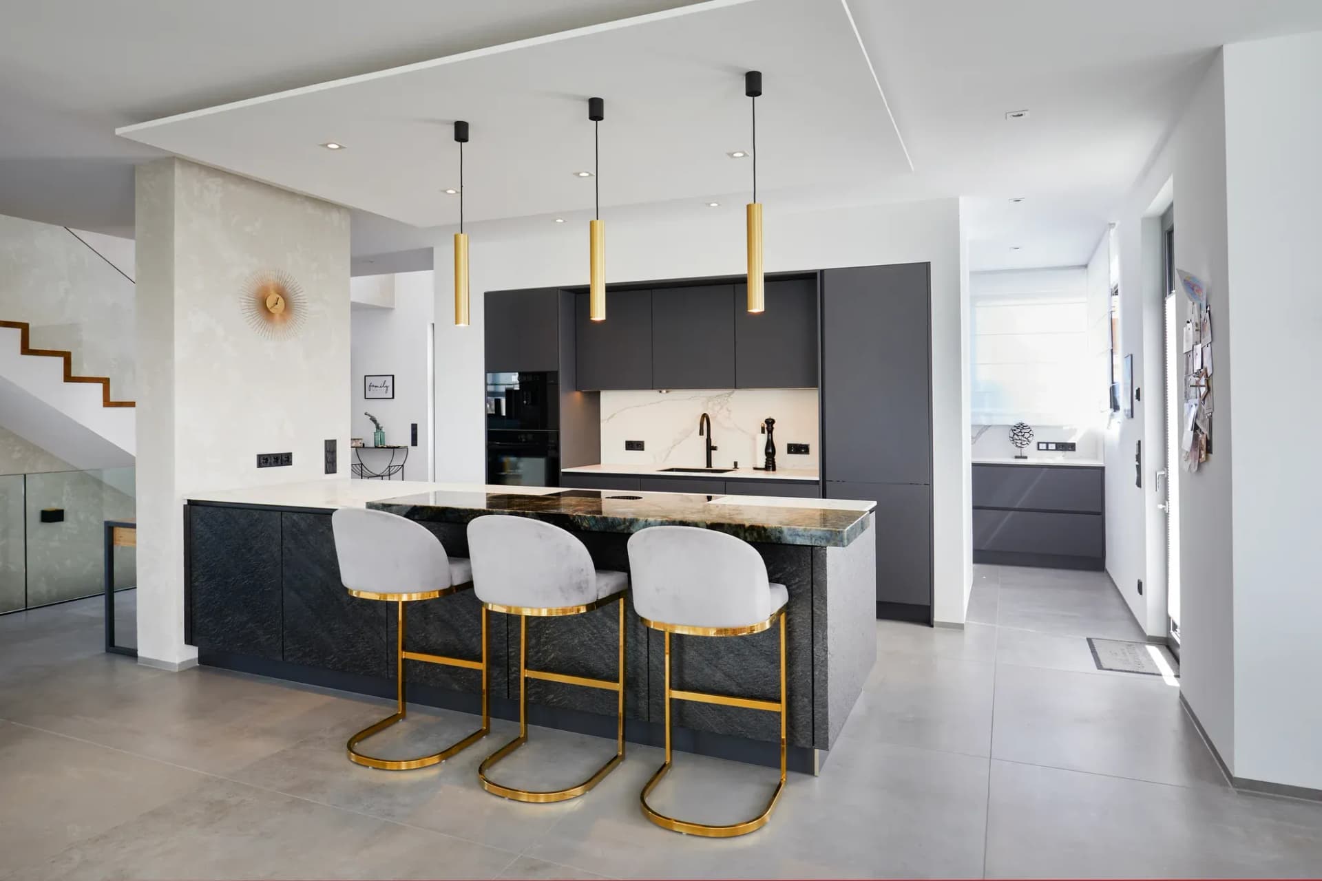 Cuisine ouverte graphite avec îlot de cuisson, suspensions dorées et tabourets de bar