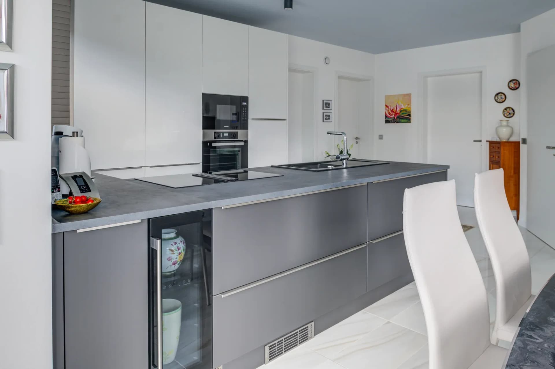 Longue rangée de cuisine en anthracite avec four encastrable, colonnes hautes blanches et plan de bar clair avec tabourets.