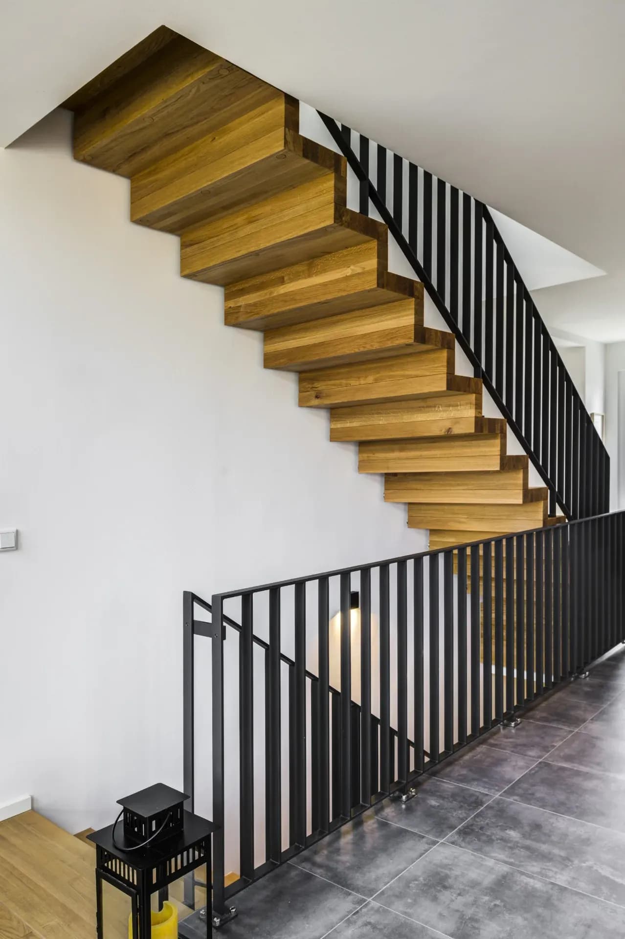 Escalier plié en chêne massif avec garde-corps à barreaux d'acier noir au-dessus d'un vide sur séjour au sol carrelé sombre