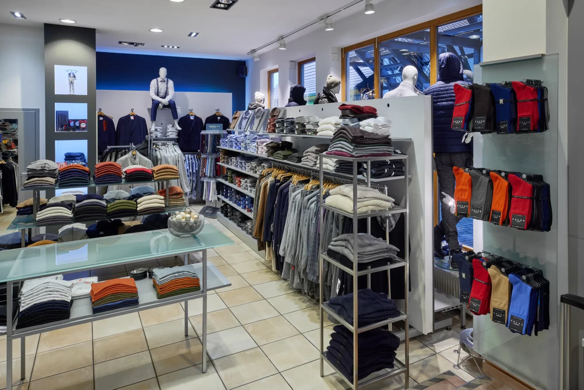 Espace de vente avec table en verre, étagères garnies de tricots pliés et portants.