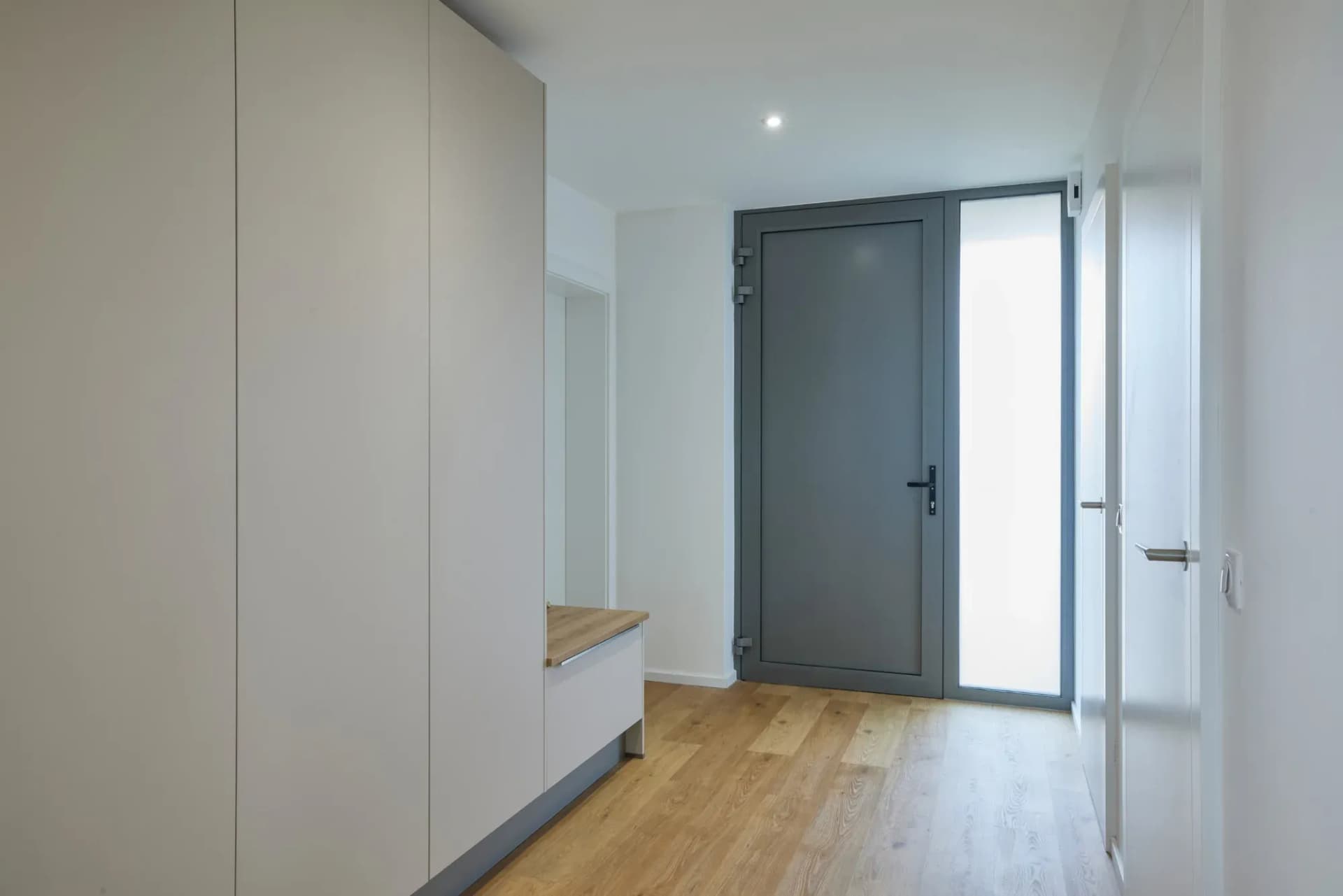 Armoire murale toute hauteur sans poignées dans l'entrée, à côté de la porte d'entrée anthracite, avec banc et miroir.
