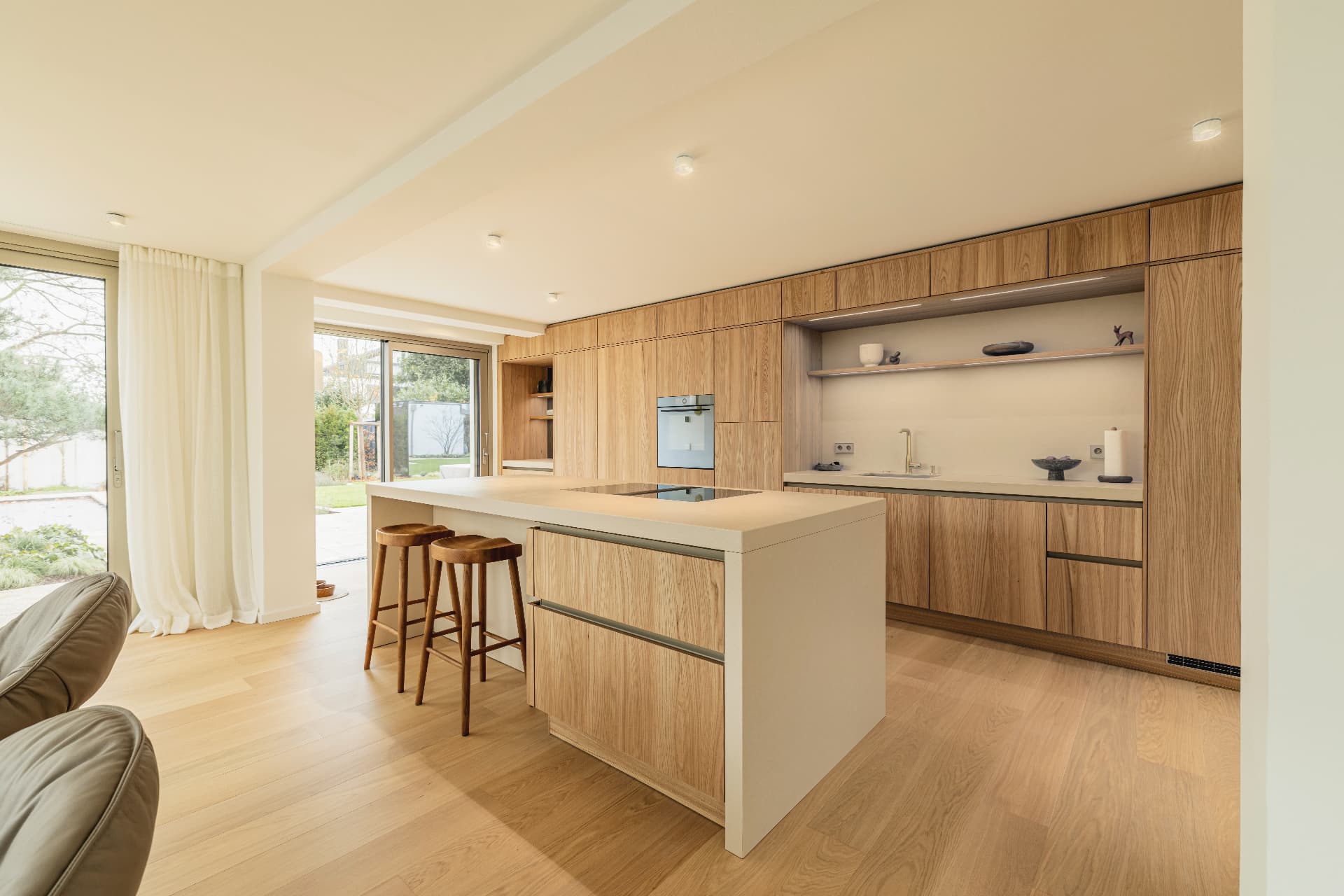 Cuisine chaleureuse avec façades en placage de chêne, plan de travail en pierre claire et vue sur le jardin