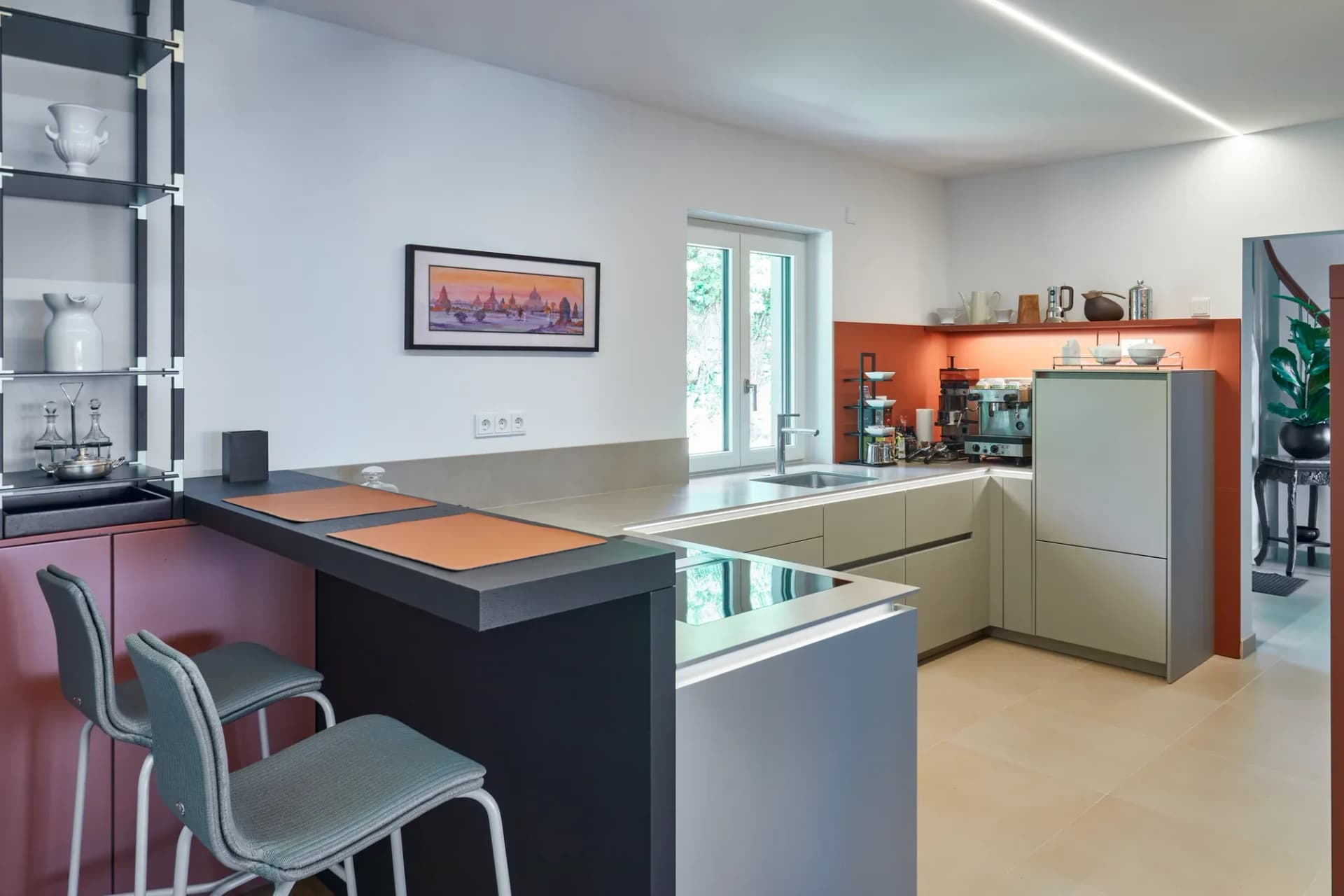 Cuisine ouverte avec bar et deux tabourets, niche murale terracotta et meubles gris-beige.