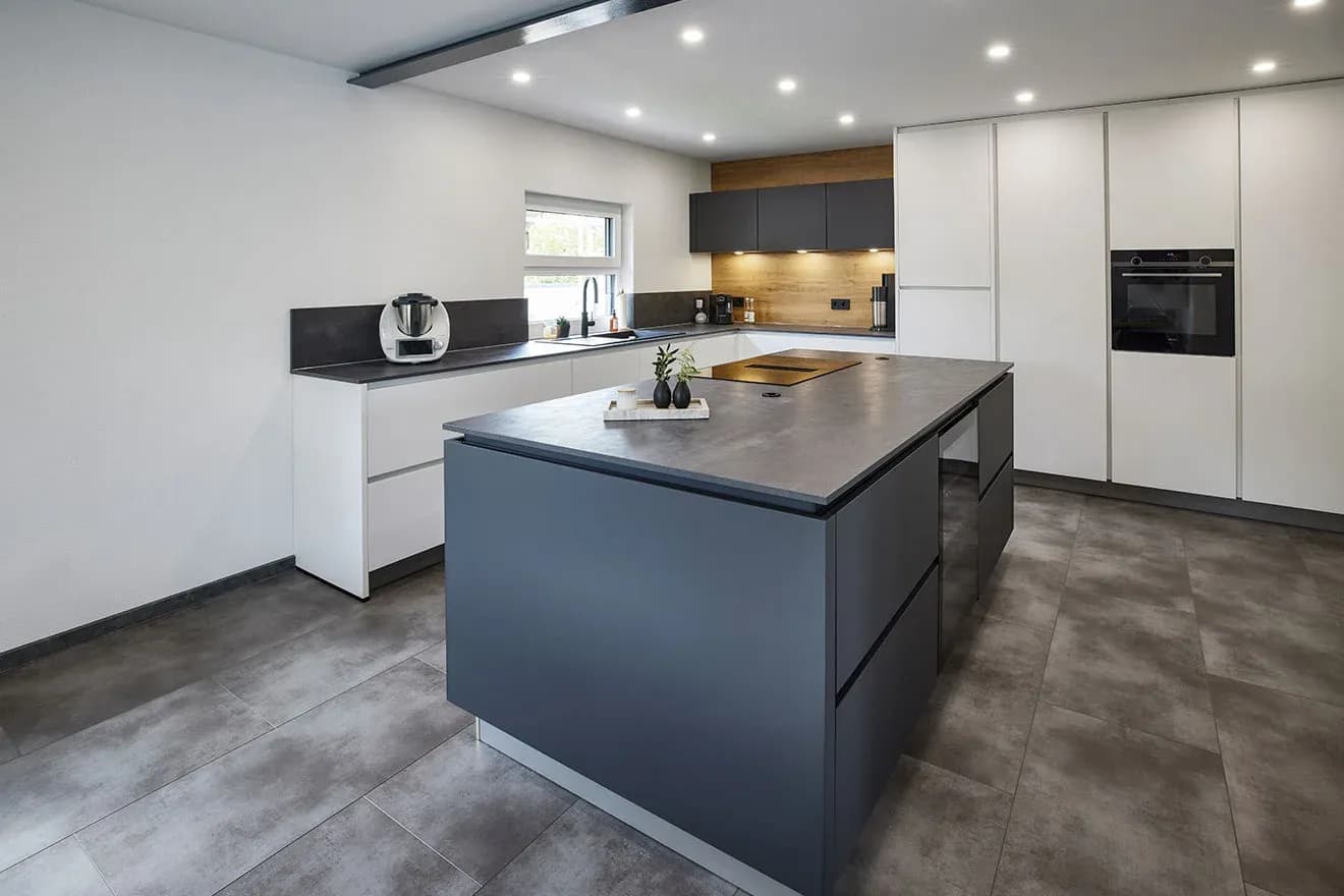 Cuisine moderne sans poignées avec îlot de cuisson anthracite, façades murales blanches claires et une niche en bois comme accent chaleureux.