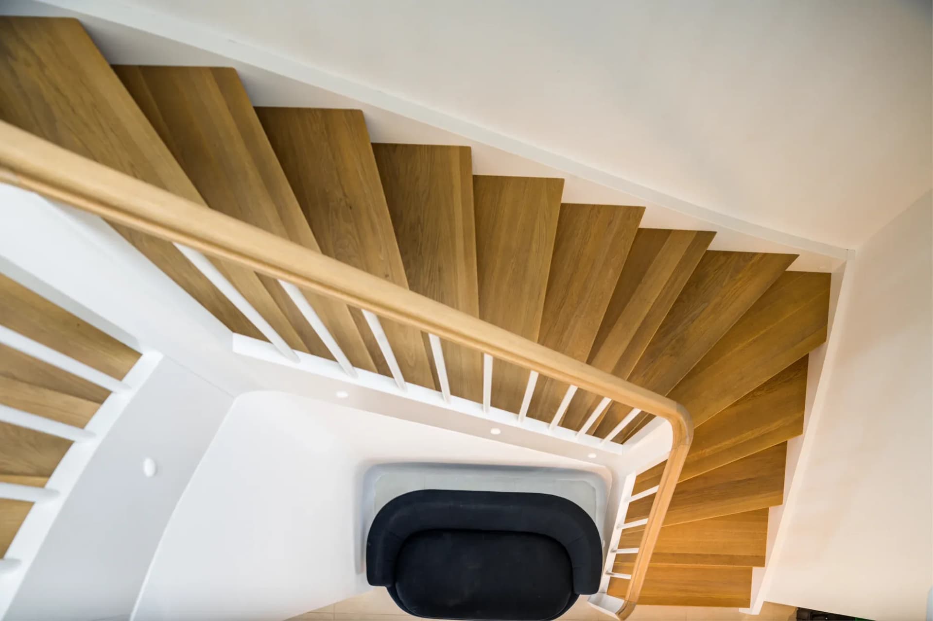 Vue plongeante dans la cage d'escalier : marches en bois massif hélicoïdales avec balustres blancs