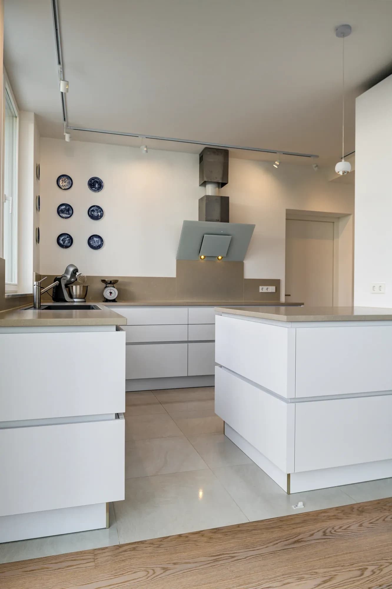 Cuisine blanche sans poignée avec îlot de cuisson indépendant et sol en parquet, vue d'ensemble