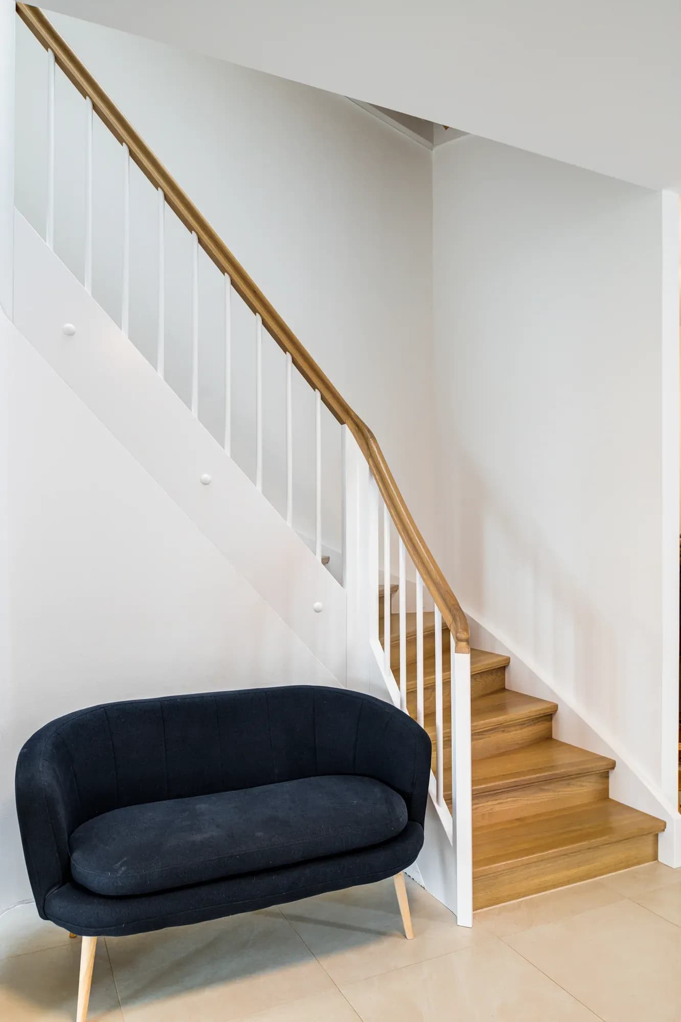 Escalier en bois massif à limons blancs dans un séjour, avec un banc sombre au premier plan