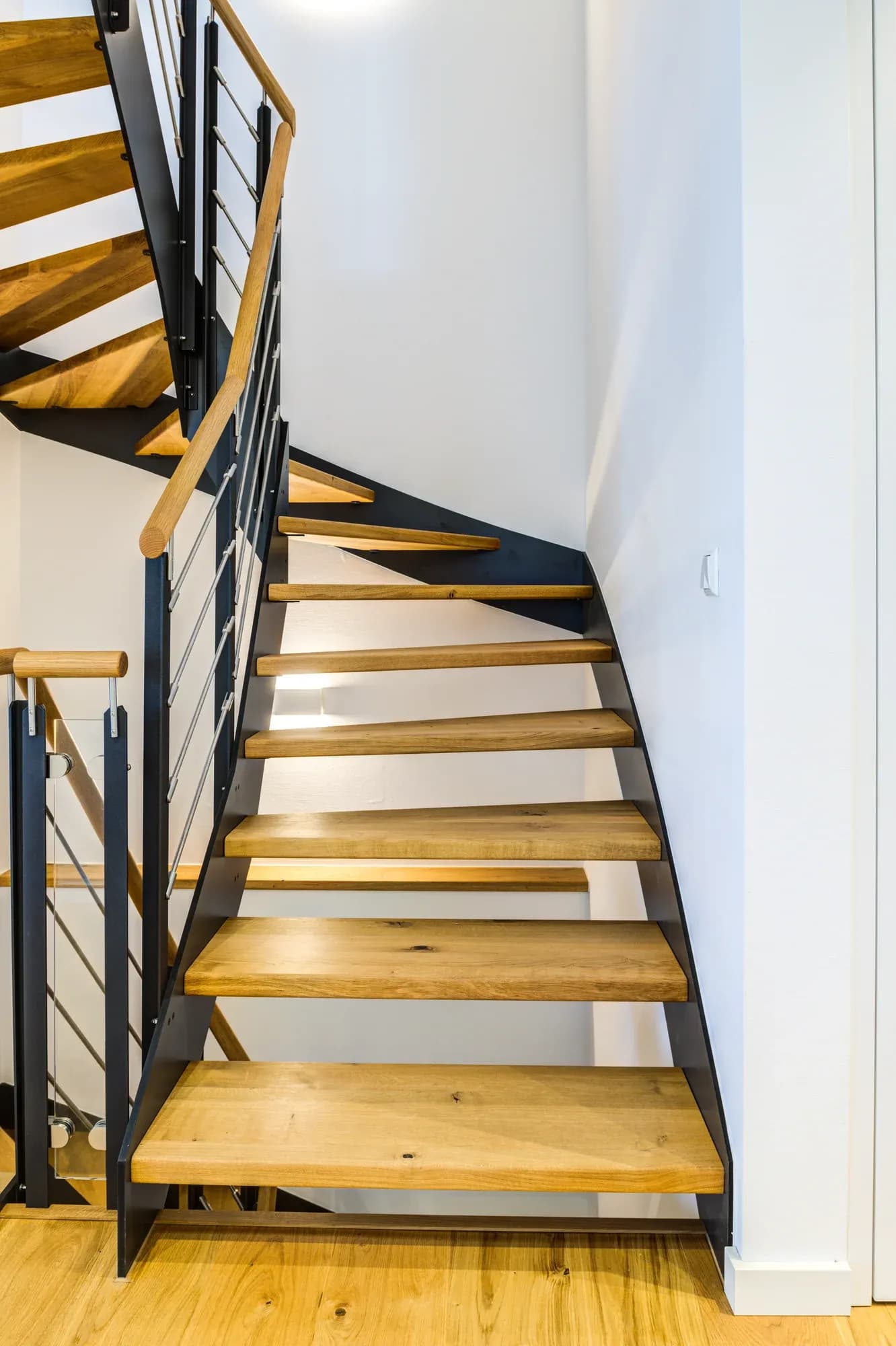 Escalier ouvert en bois massif : marches en chêne sur limons en acier noir, garde-corps en inox et main courante en chêne, avec éclairage LED sous les marches.