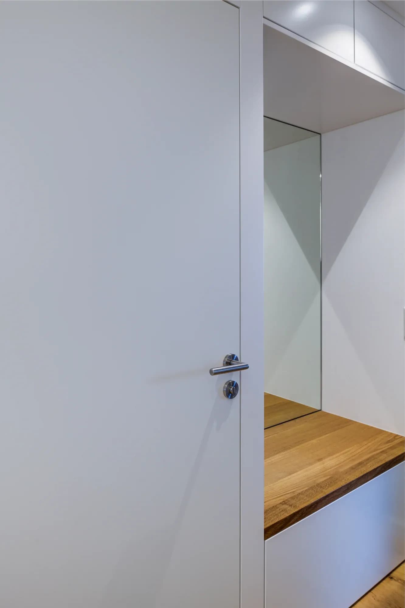 Niche de vestiaire avec grand miroir, placard blanc et banc à plateau en chêne massif.