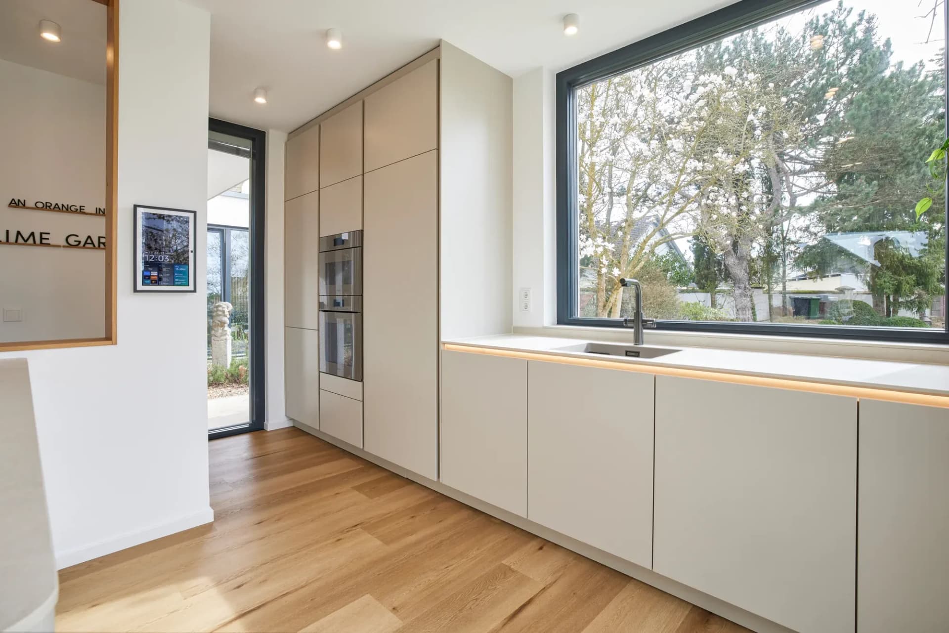 Rangée de cuisine près de la fenêtre avec plan de travail clair en pierre naturelle, évier sous plan et robinetterie noire, vue sur le jardin.