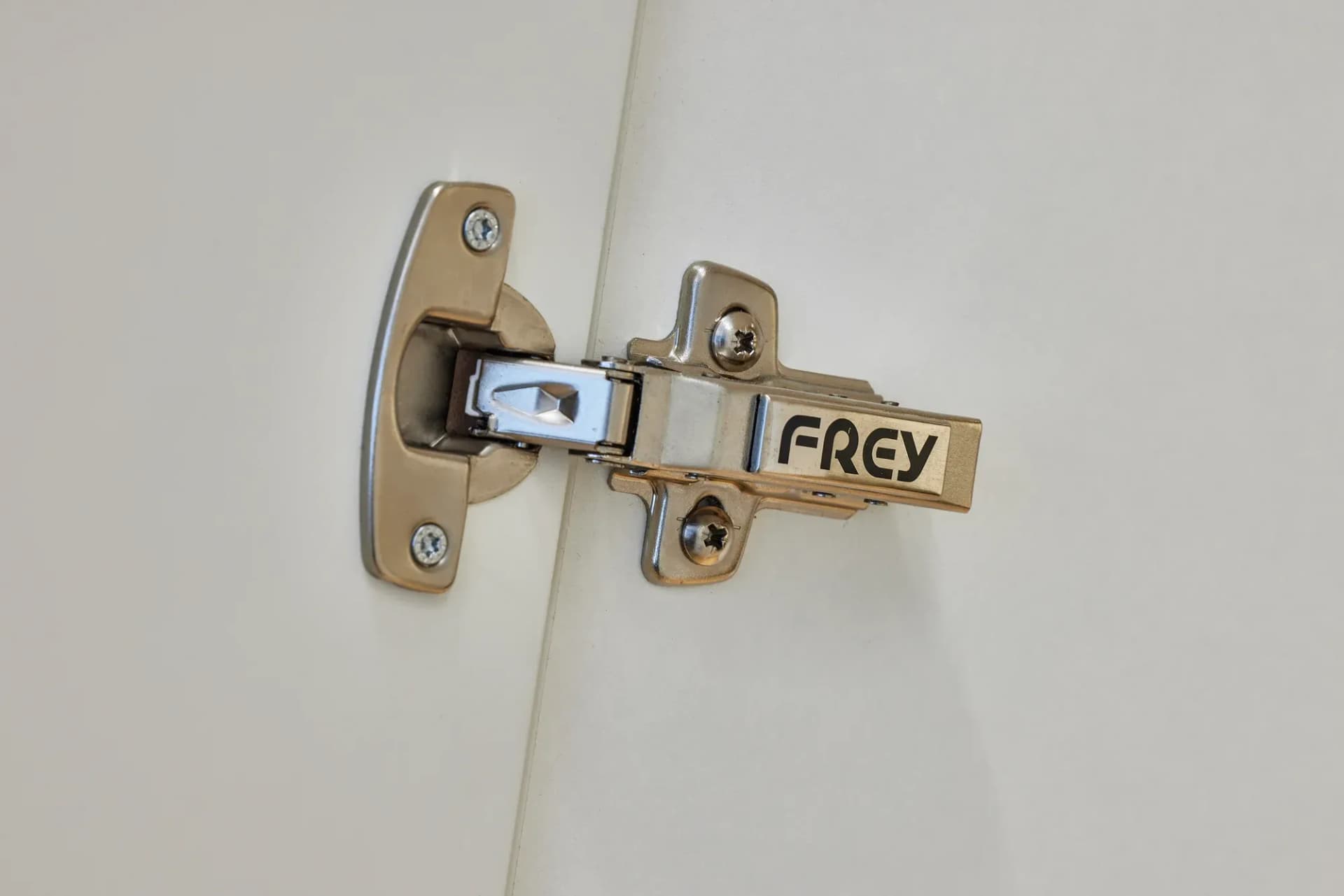 Détail d'une charnière de meuble gravée FREY sur une façade d'armoire blanche.