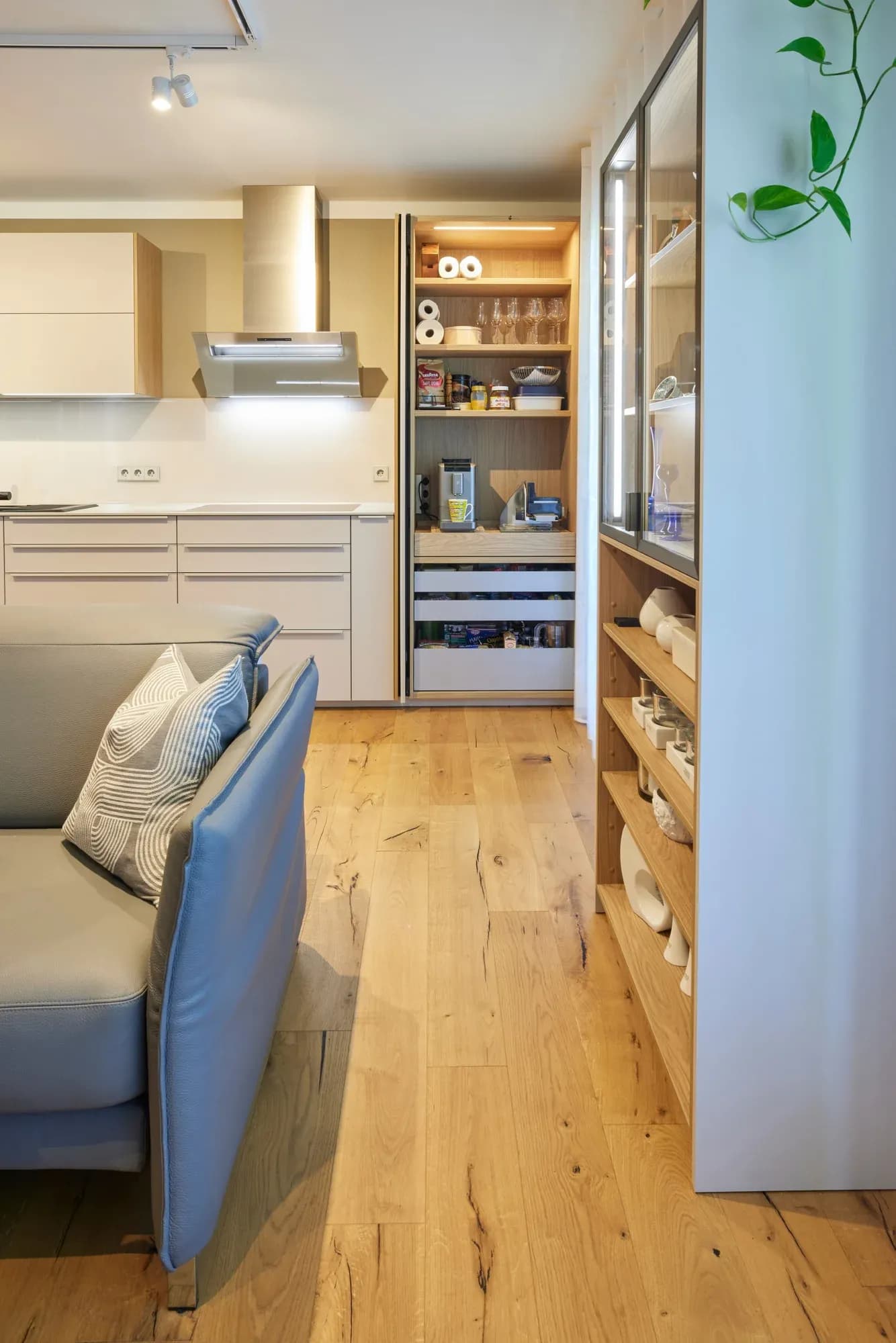 Mur de colonnes ouvert avec niche garde-manger : tiroirs, coin petit-déjeuner et tablettes en chêne noueux ; à droite, la vitrine en verre séparant l'espace, à tablettes en chêne.