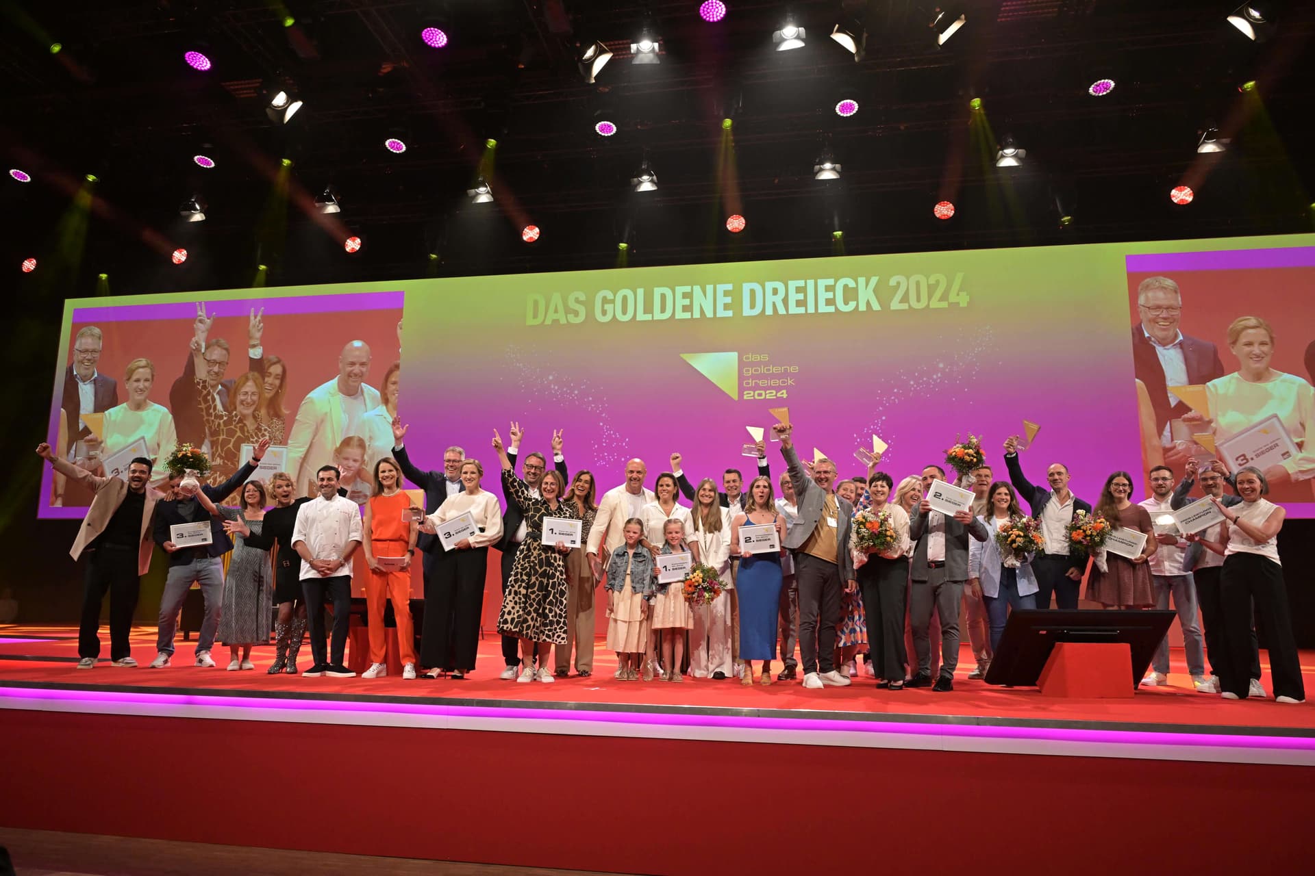 Remise des prix « Das Goldene Dreieck 2024 » sur scène : les équipes gagnantes avec certificats et trophées devant l'écran de scène
