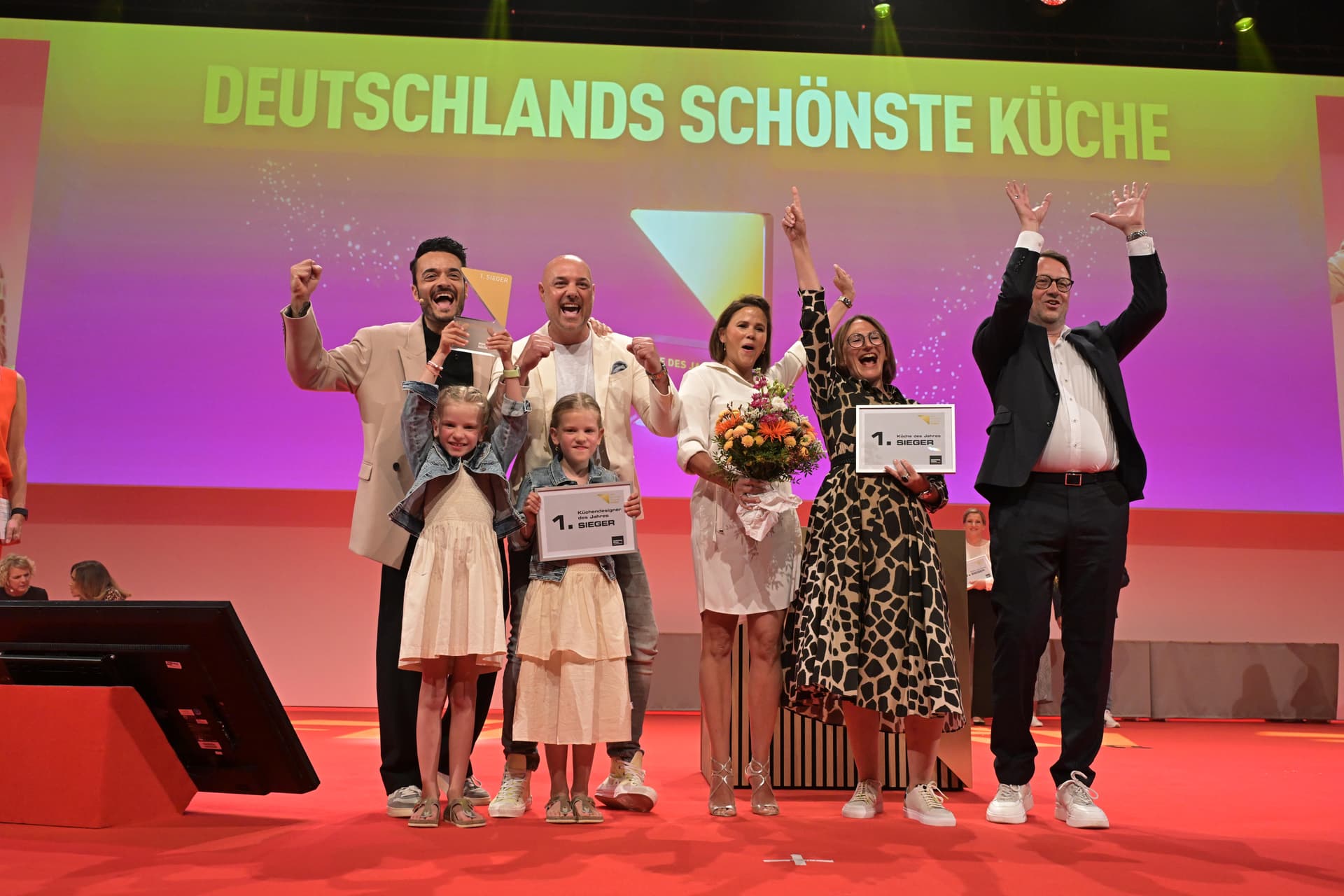 Moment sur scène lors de la remise du prix « La plus belle cuisine d'Allemagne » : la famille Tews avec l'équipe Frey, entourée de diplômes « 1er prix » et d'un bouquet de fleurs