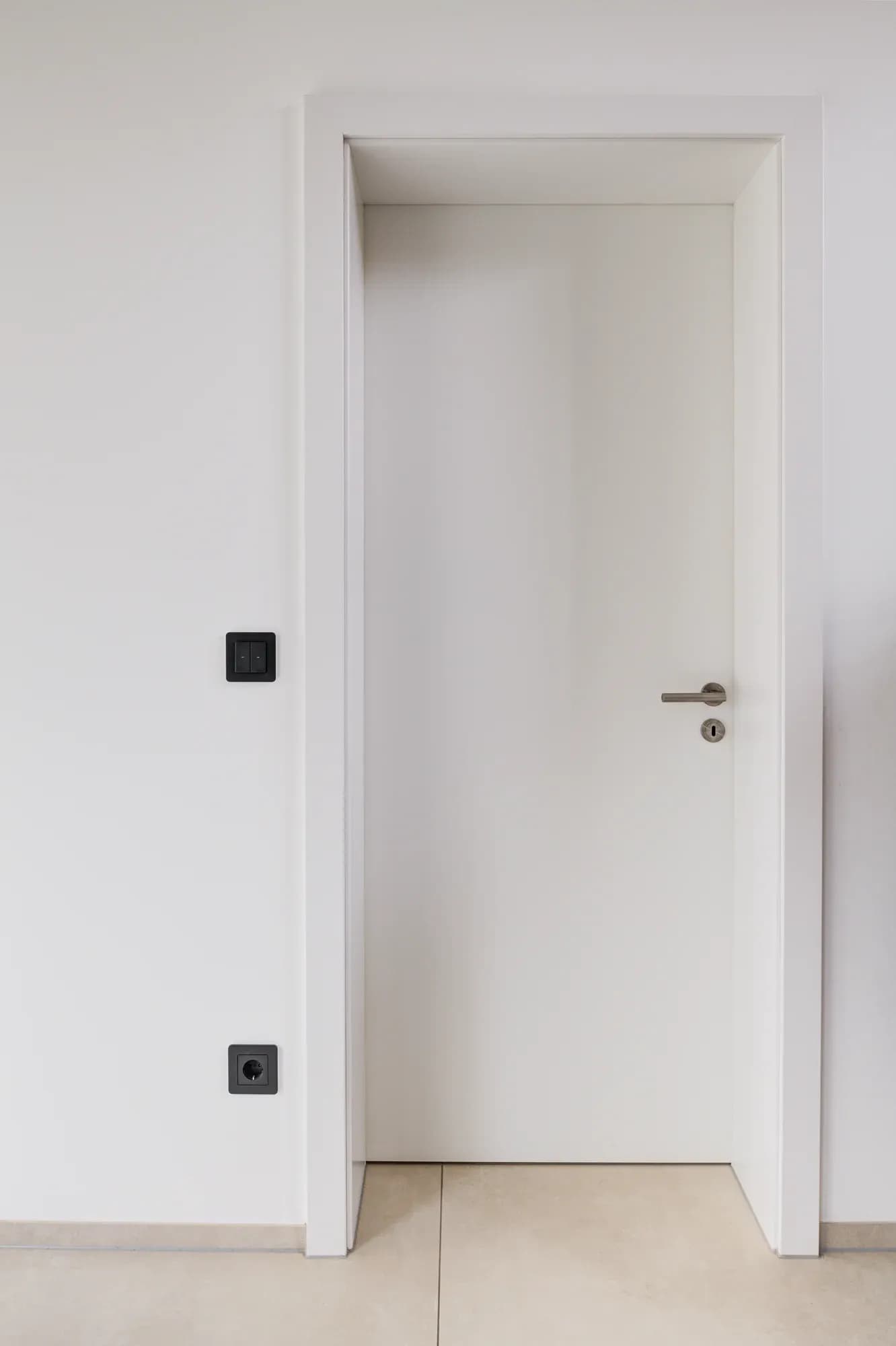Porte intérieure blanche fermée, sans poignée apparente, avec fine poignée métallique, affleurante dans un mur lisse.